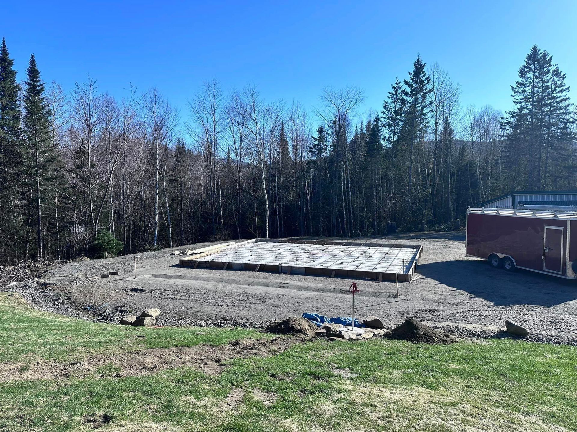 A red trailer is parked in a dirt field with trees in the background