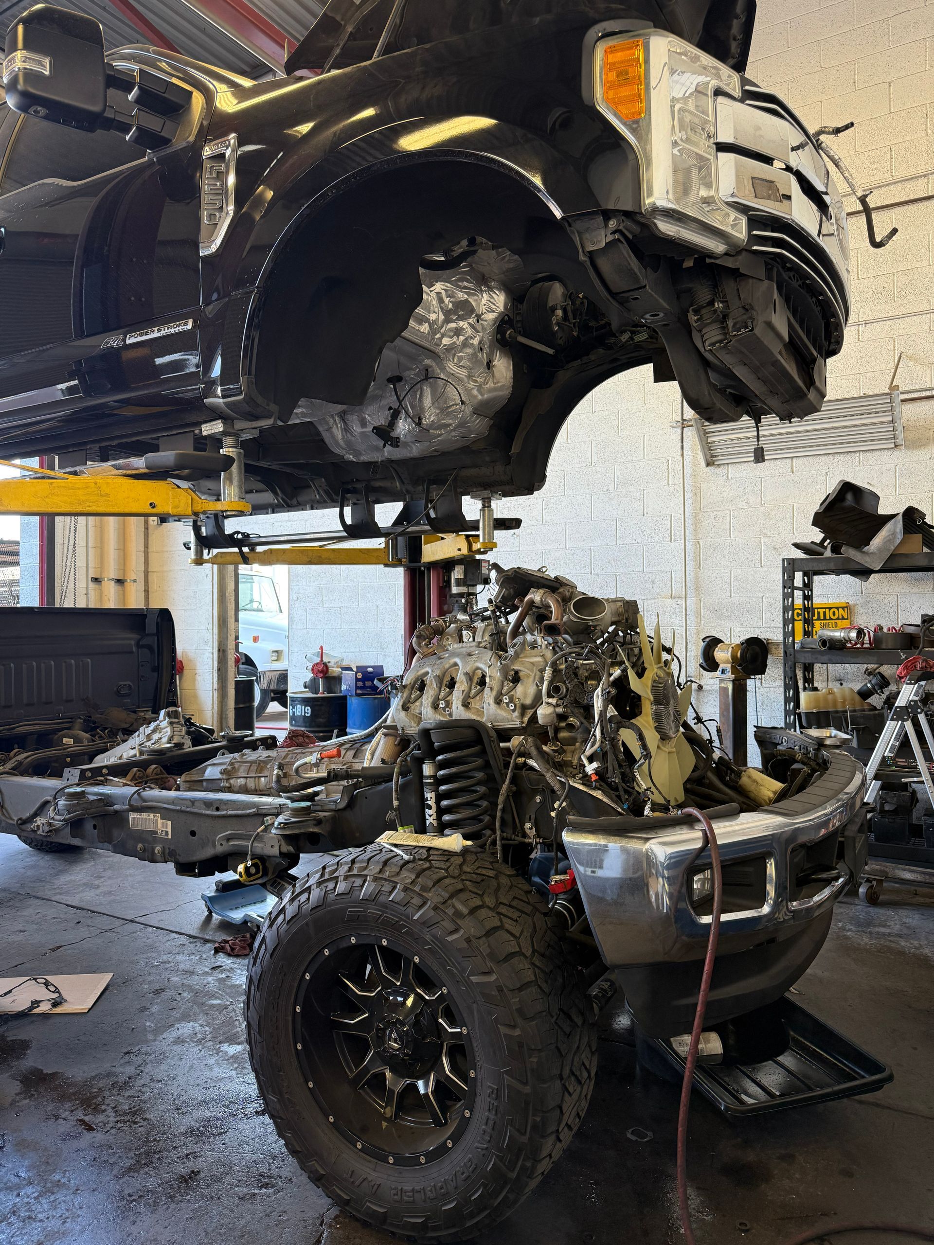 Truck undergoing repairs in a shop, the body suspended above the chassis with exposed engine.