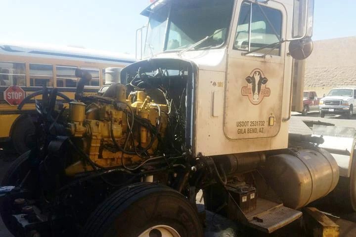 A white semi-truck with the hood open, revealing a yellow engine, parked next to a yellow school bus.