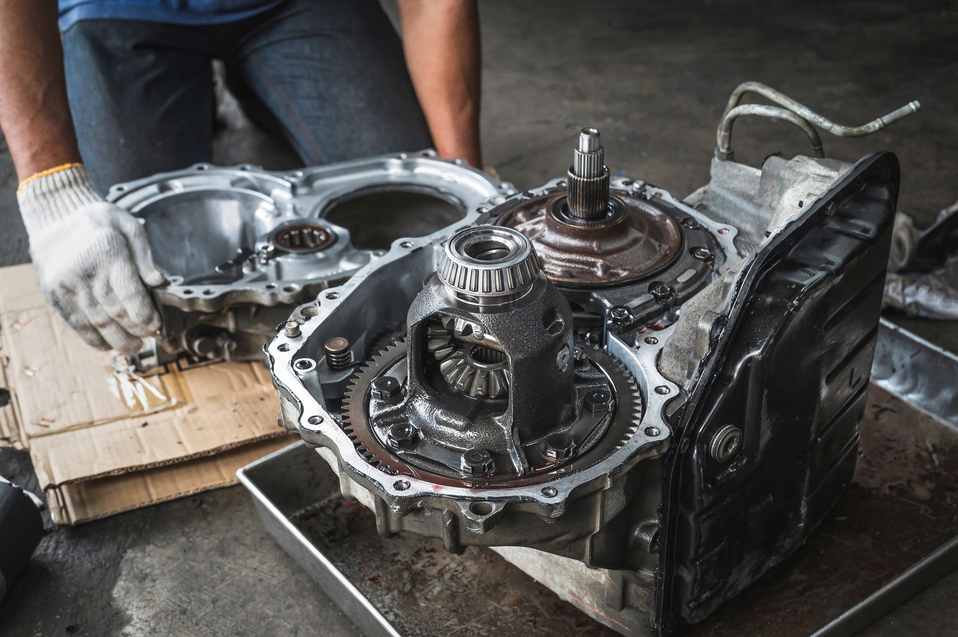 Person disassembling a car transmission, oily metal components visible.