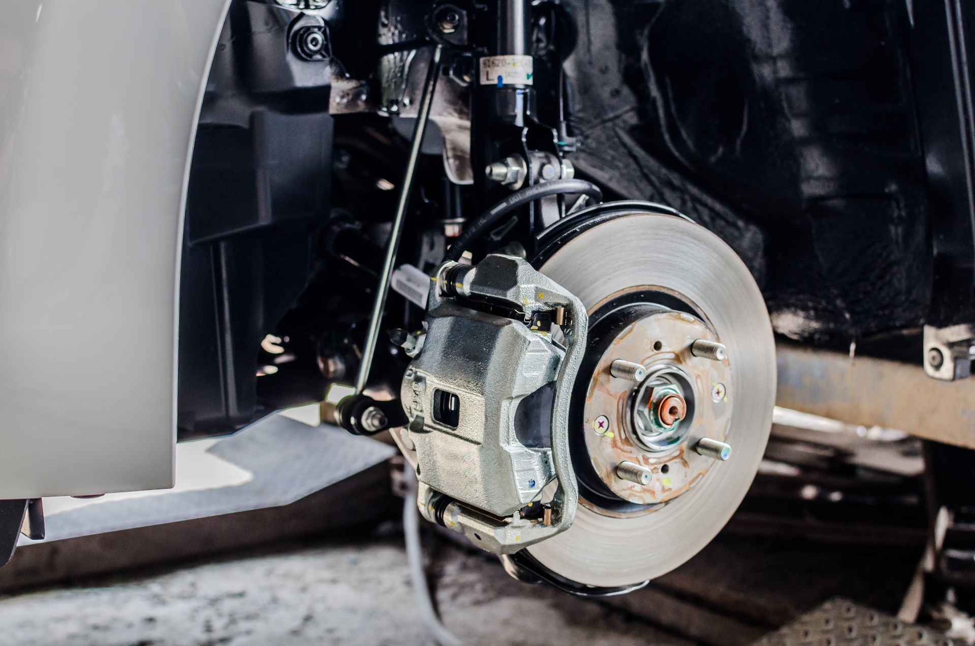 Car brake disc and caliper assembly, silver disc with black and silver components in workshop.