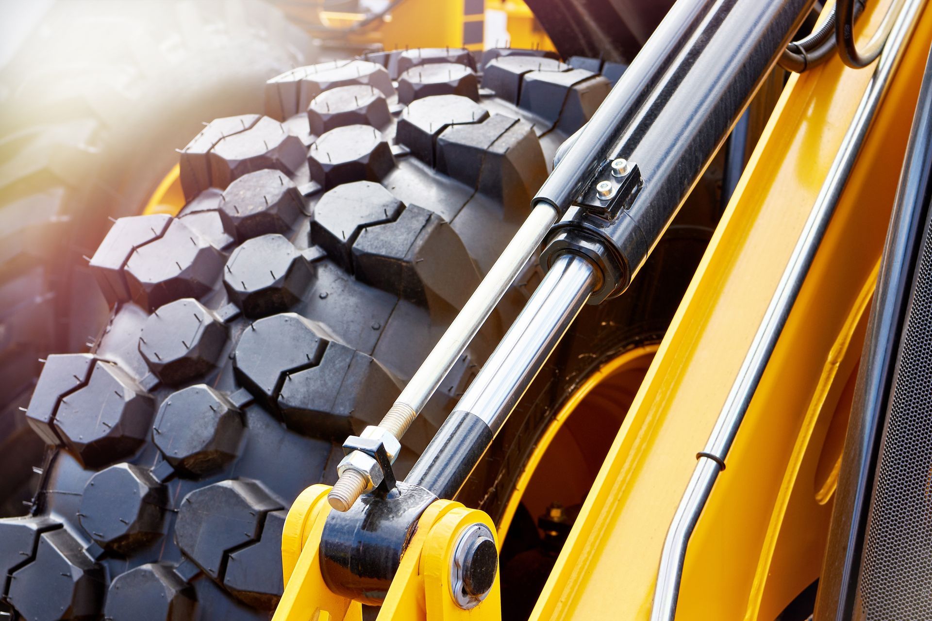 Close-up of a heavy construction vehicle tire and hydraulic cylinder; yellow and black.
