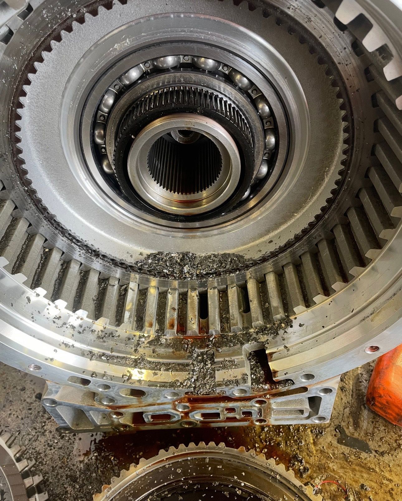 Damaged transmission component, metal shavings visible around gears and bearings.