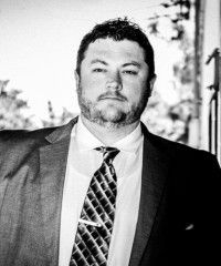 Man in suit and tie looking directly at the camera, with a serious expression.
