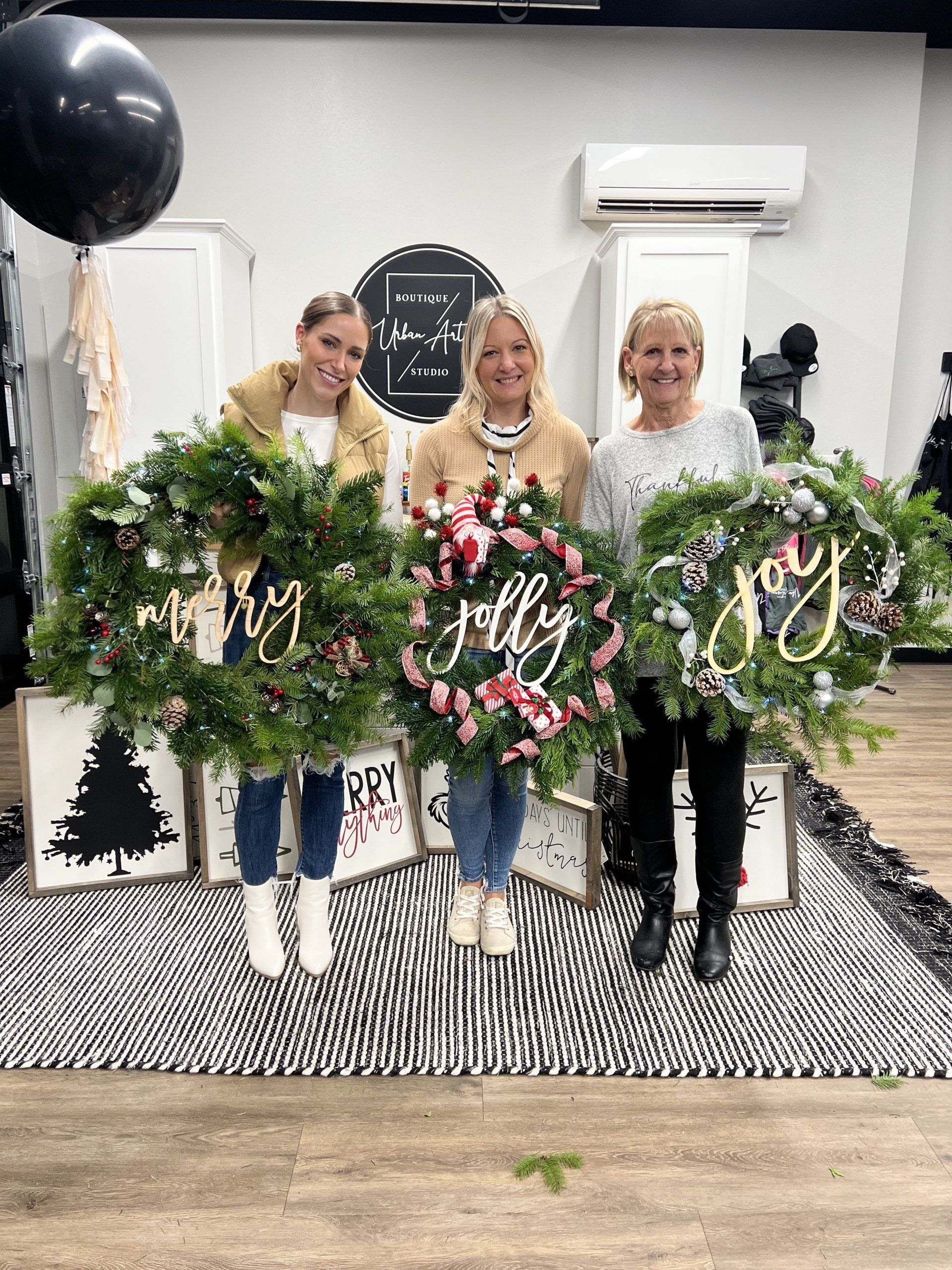 Three women are holding christmas wreaths in a room.