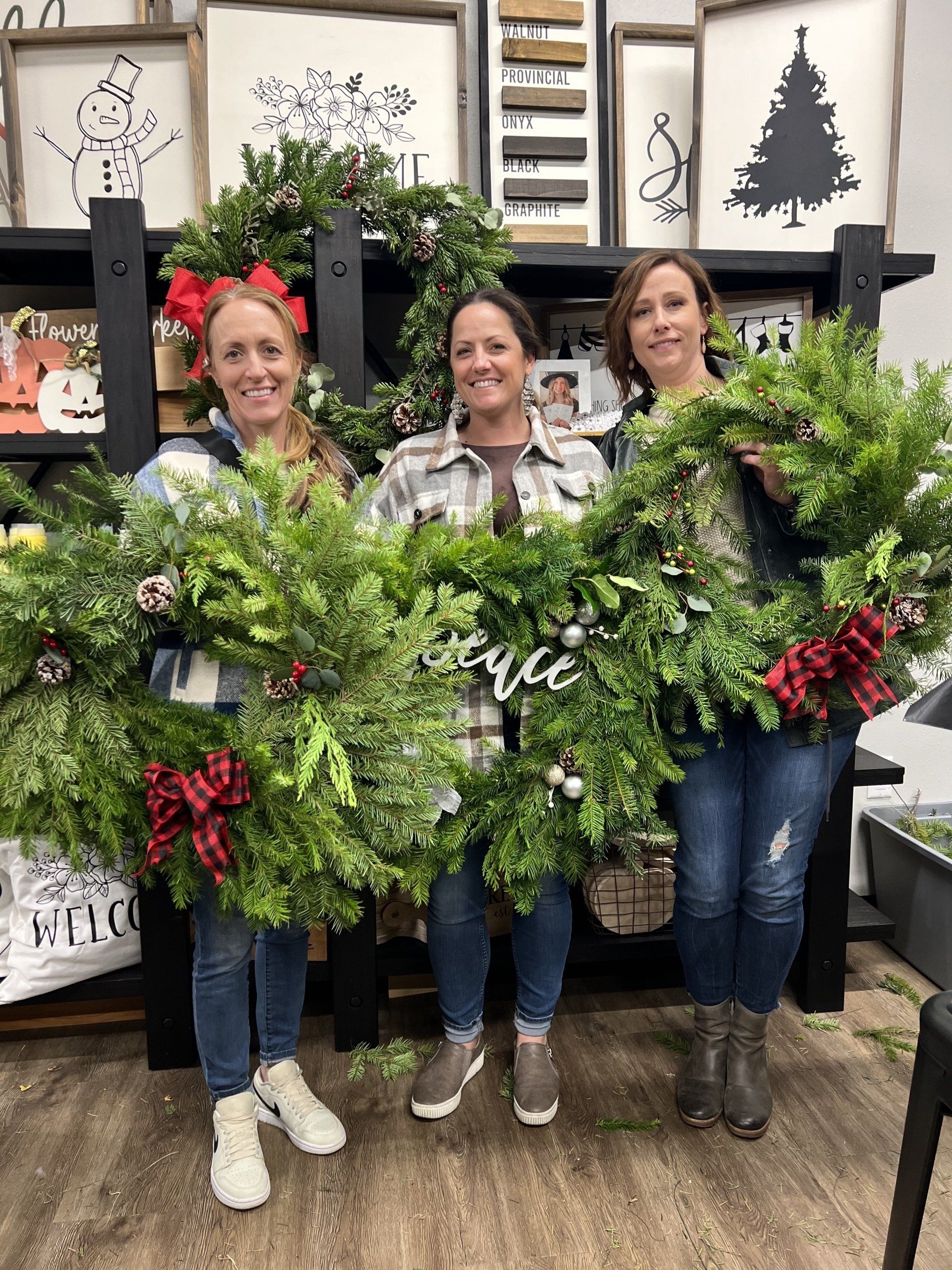 Three women are holding christmas wreaths in a store.