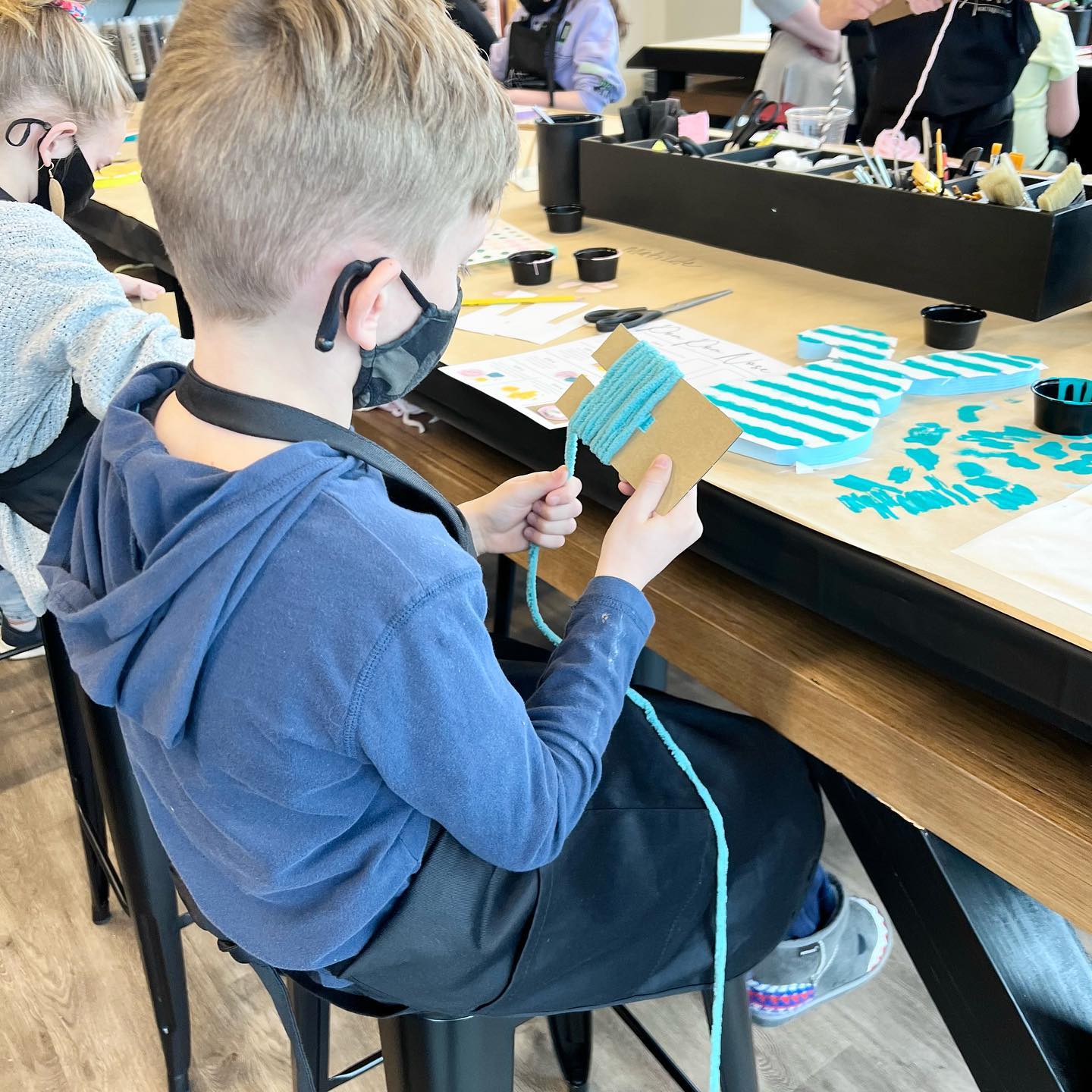 A boy wearing a mask is sitting at a table holding a piece of paper.