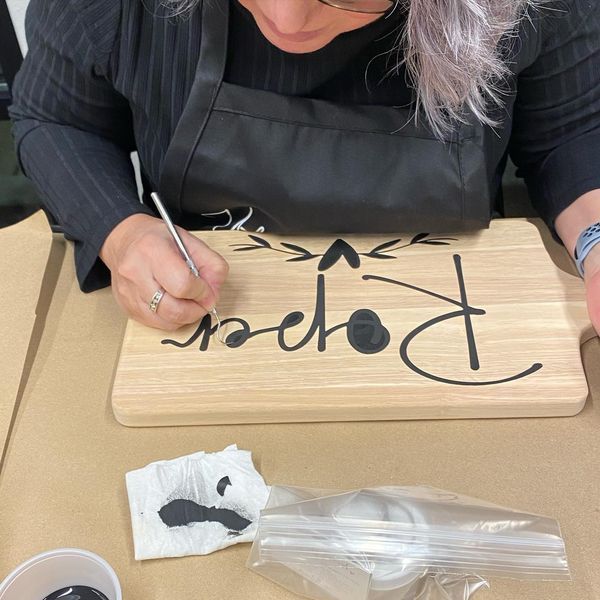 A woman in an apron is writing on a wooden cutting board