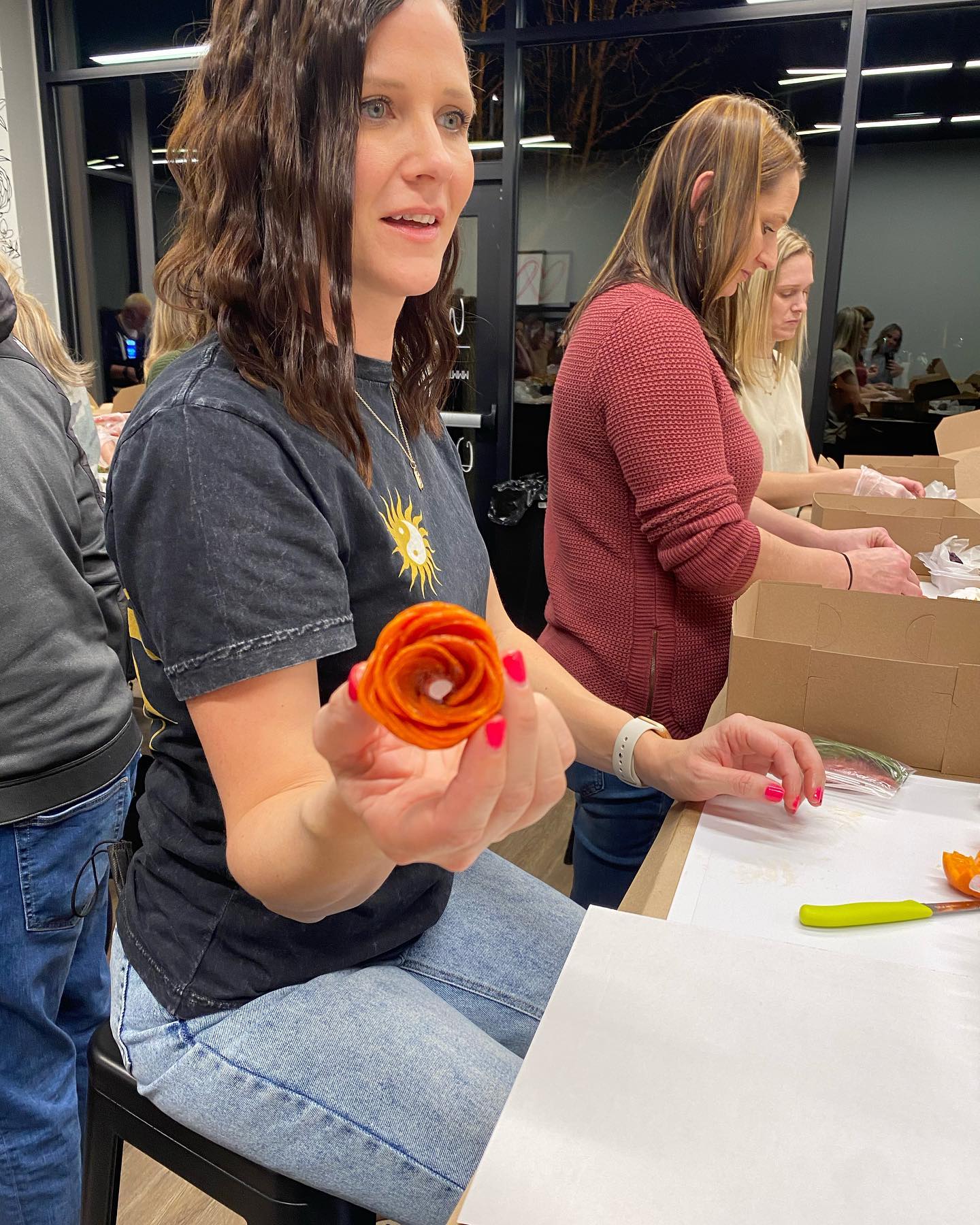 A woman is sitting at a table holding an orange flower.