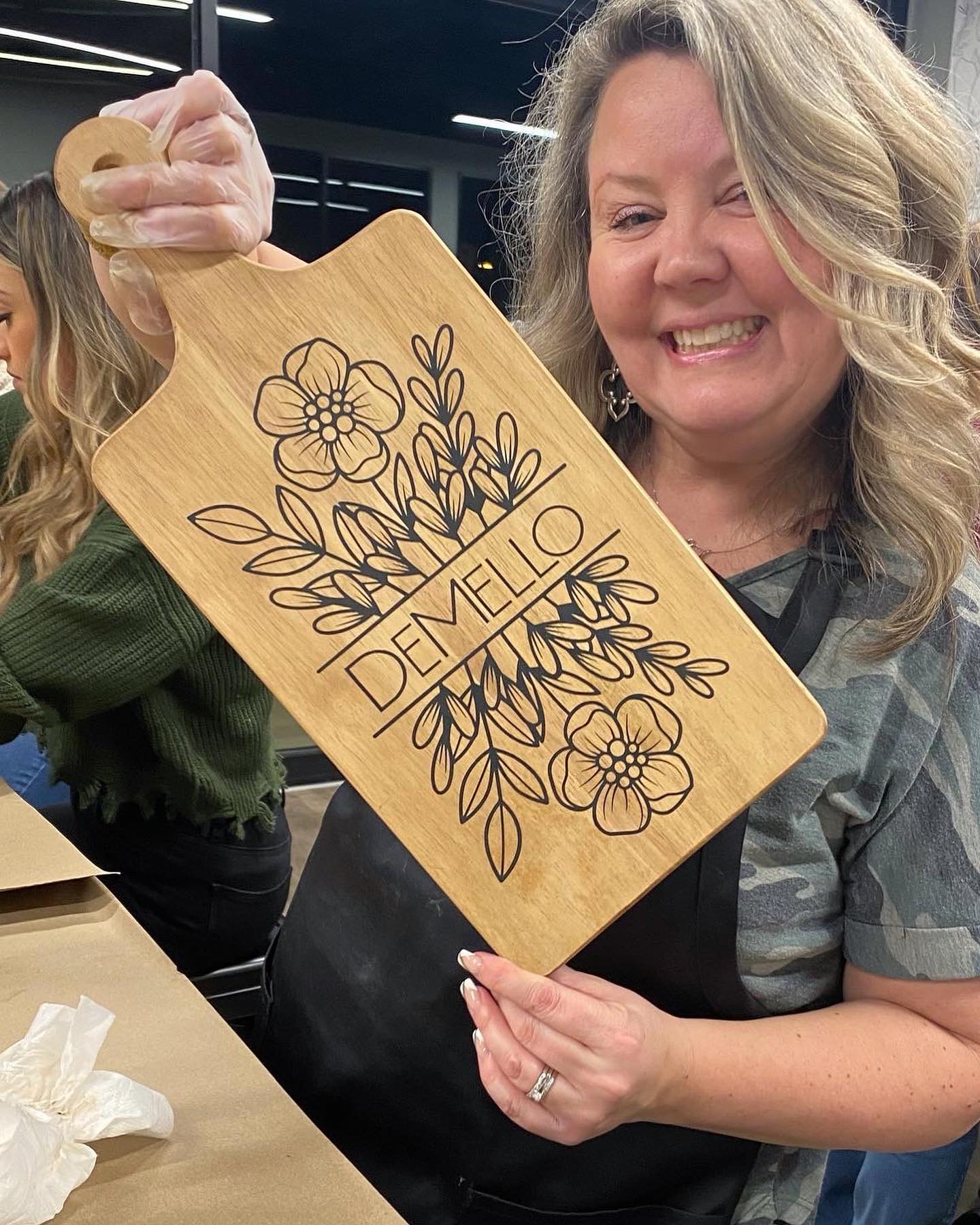 A woman is holding a wooden cutting board with flowers on it.