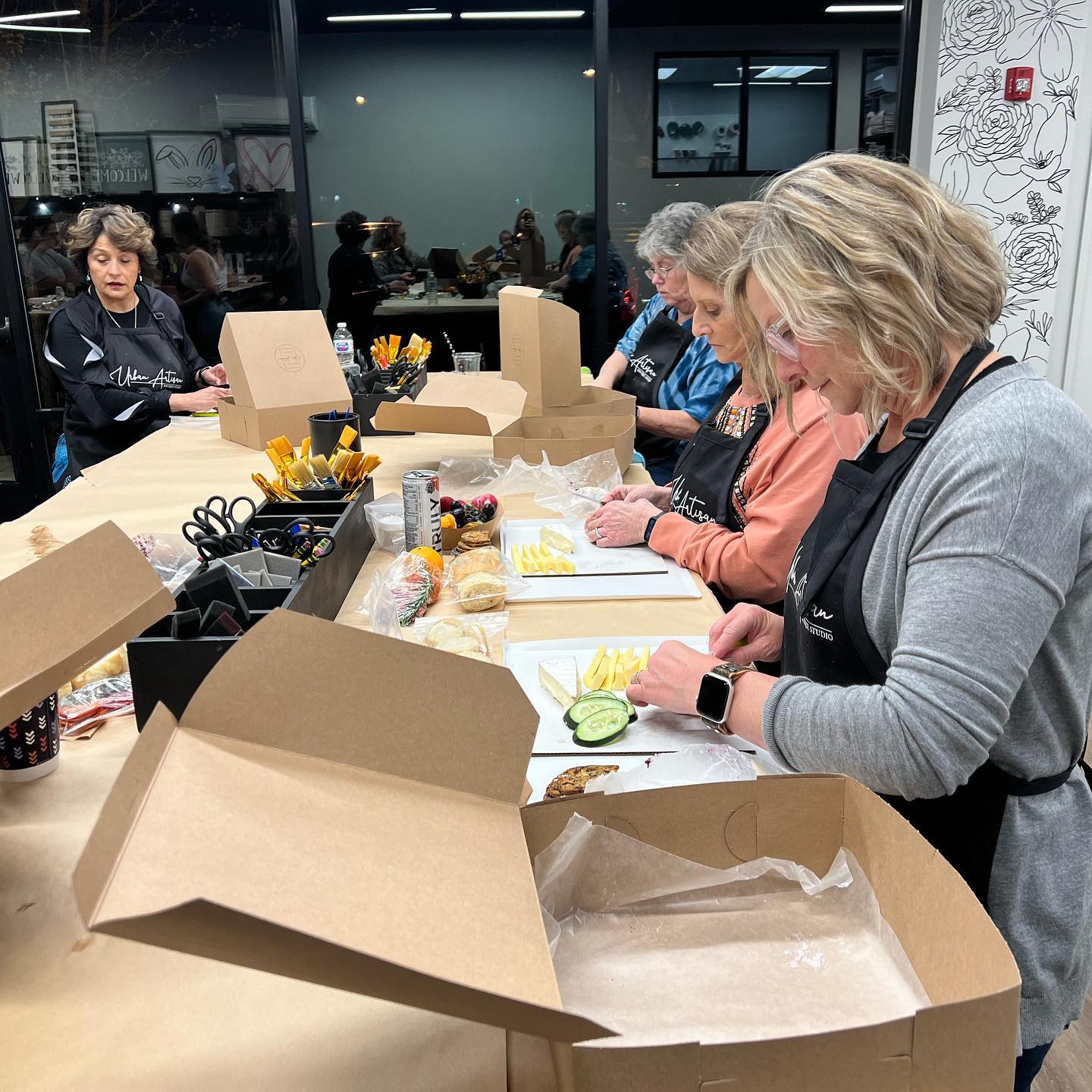 A group of women are sitting at a table with boxes of food.