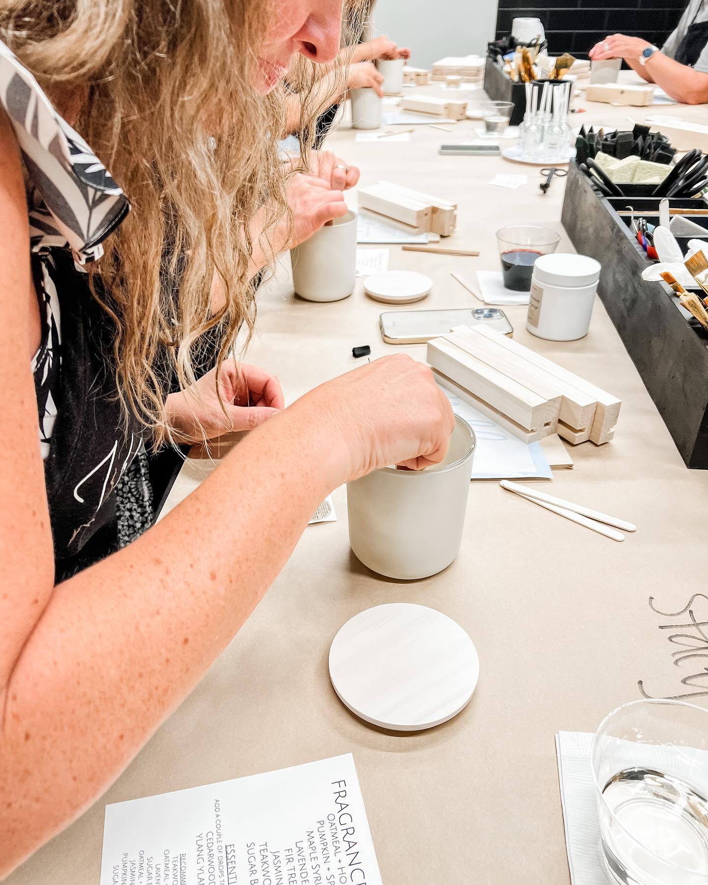 A group of people are sitting at a table making candles.