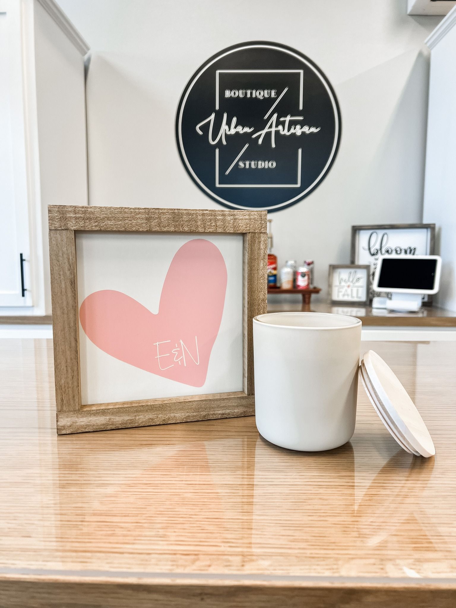 A framed picture of a pink heart is sitting on a counter next to a candle.