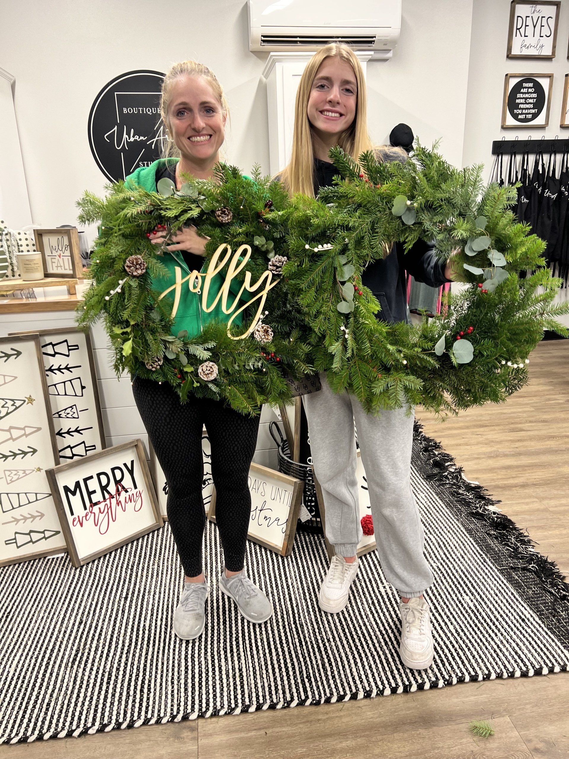 Two women are holding christmas wreaths in a store.