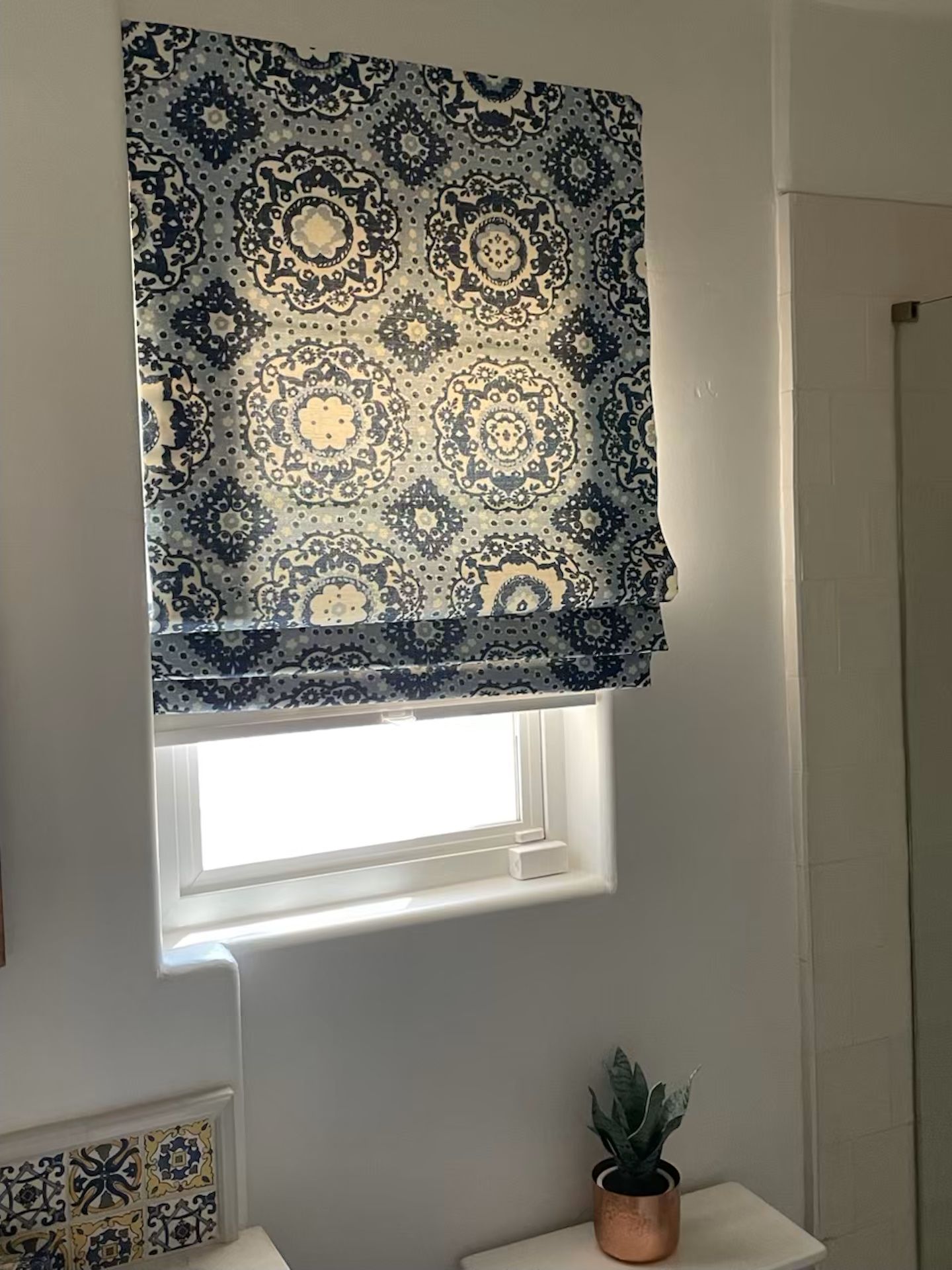 A blue and white roman shade is hanging on a window in a bathroom.