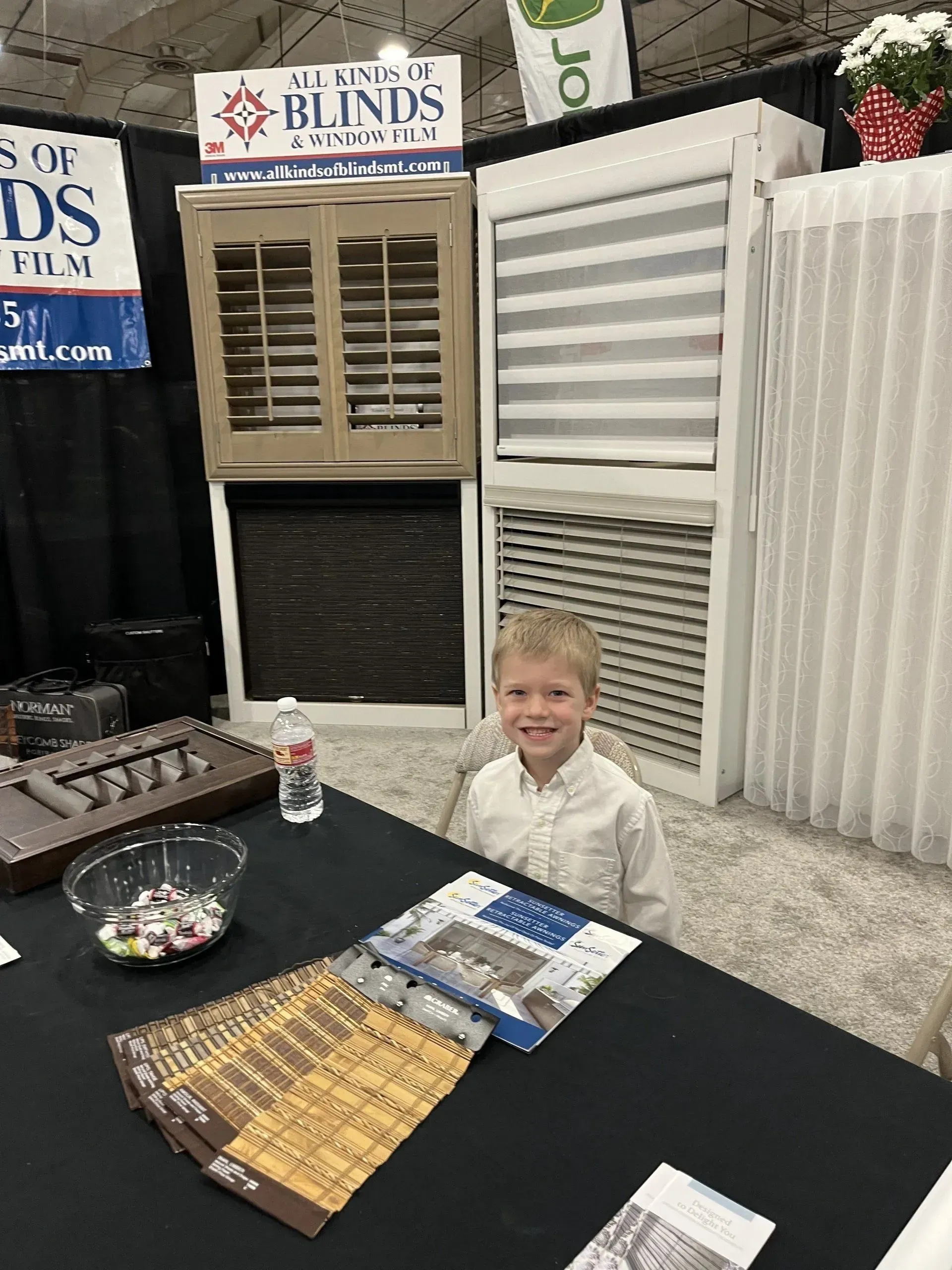 A young boy is sitting at a table in front of a display of blinds.