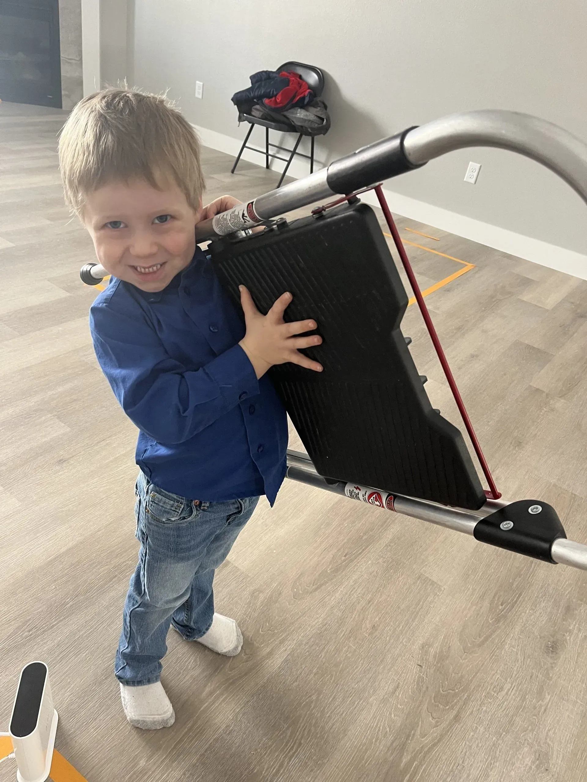 A young boy is standing next to a stroller in a living room.