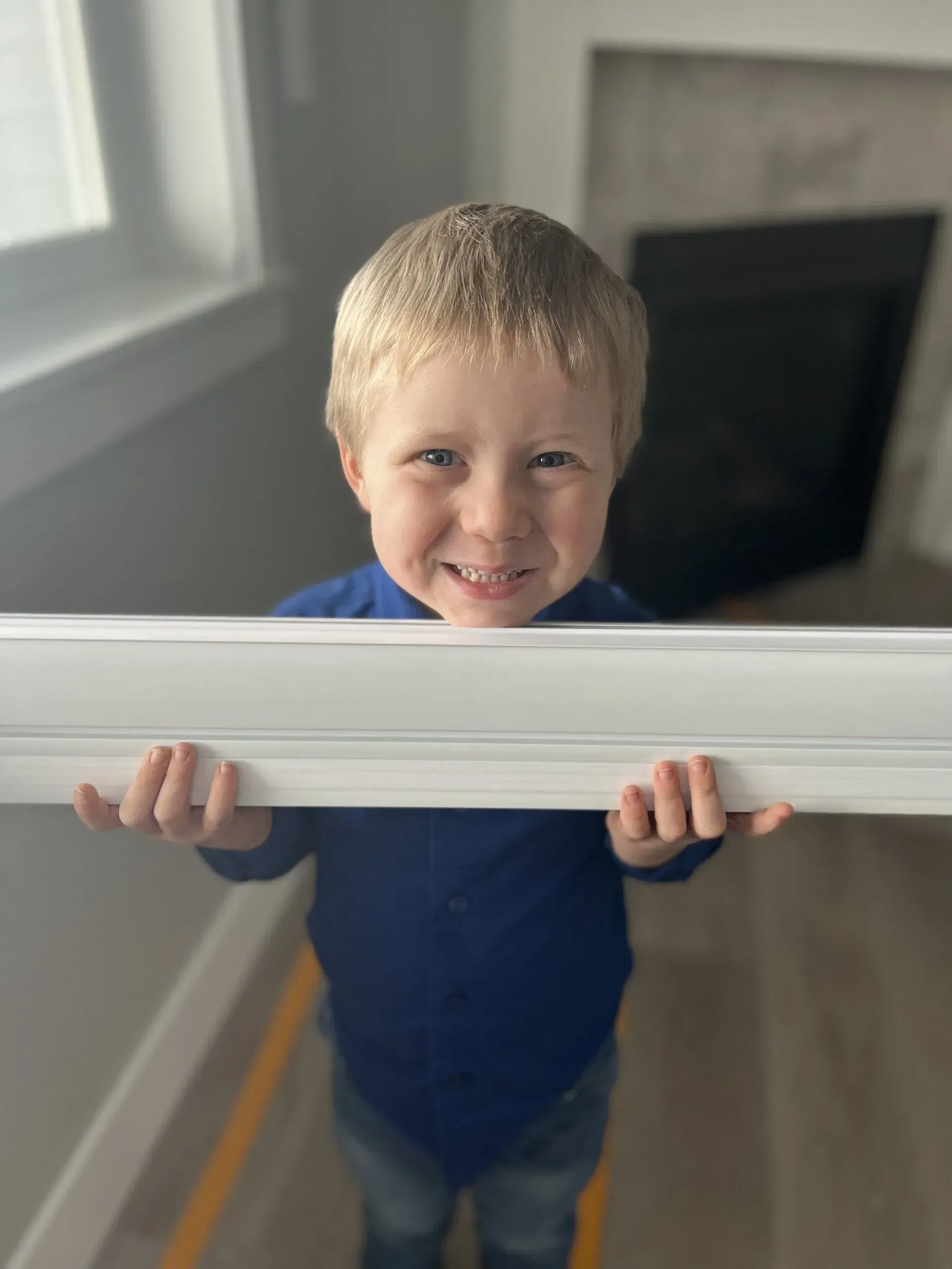 A young boy is holding a white picture frame in his hands.