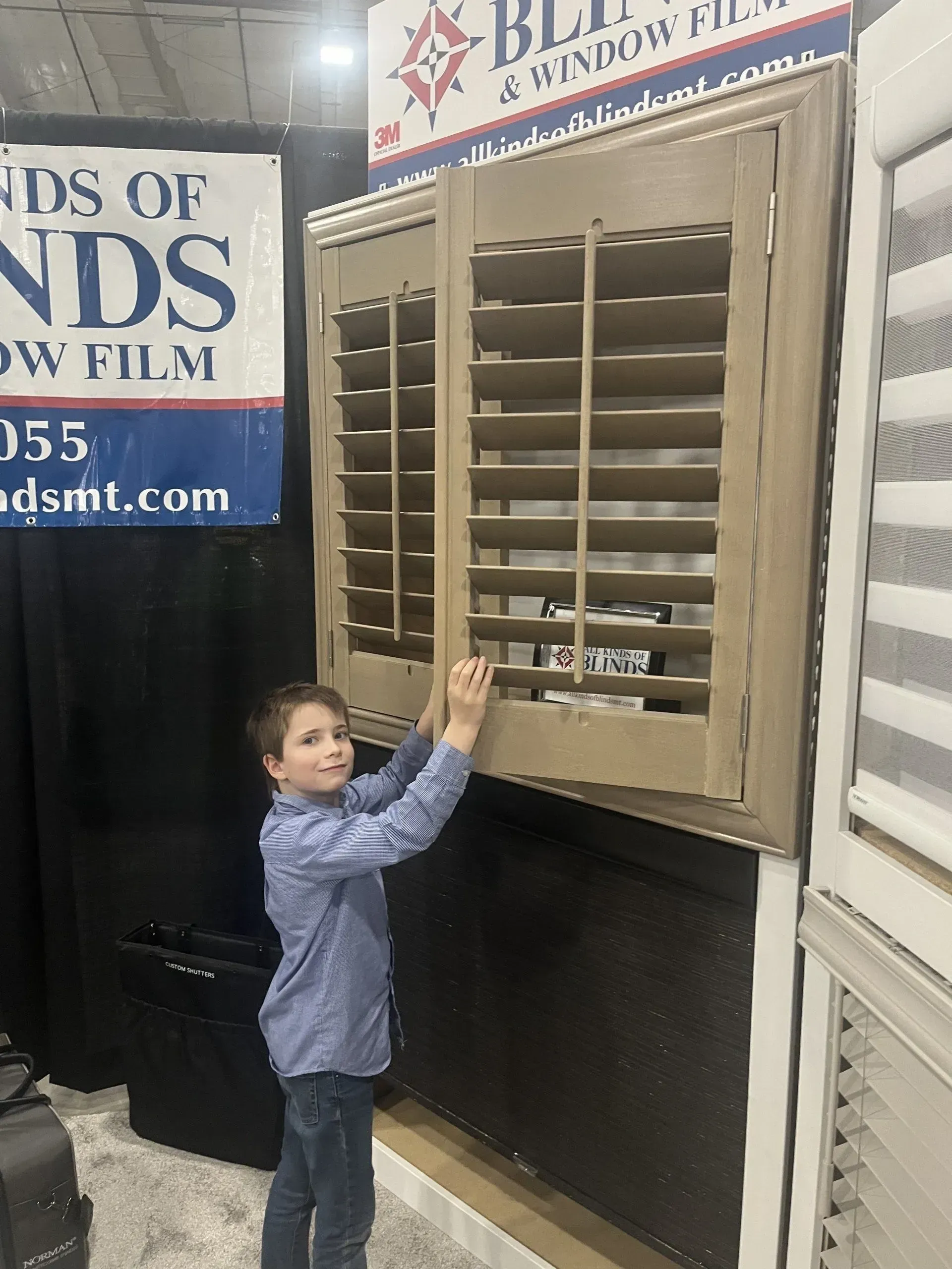A young boy is opening a window shutter in a store.