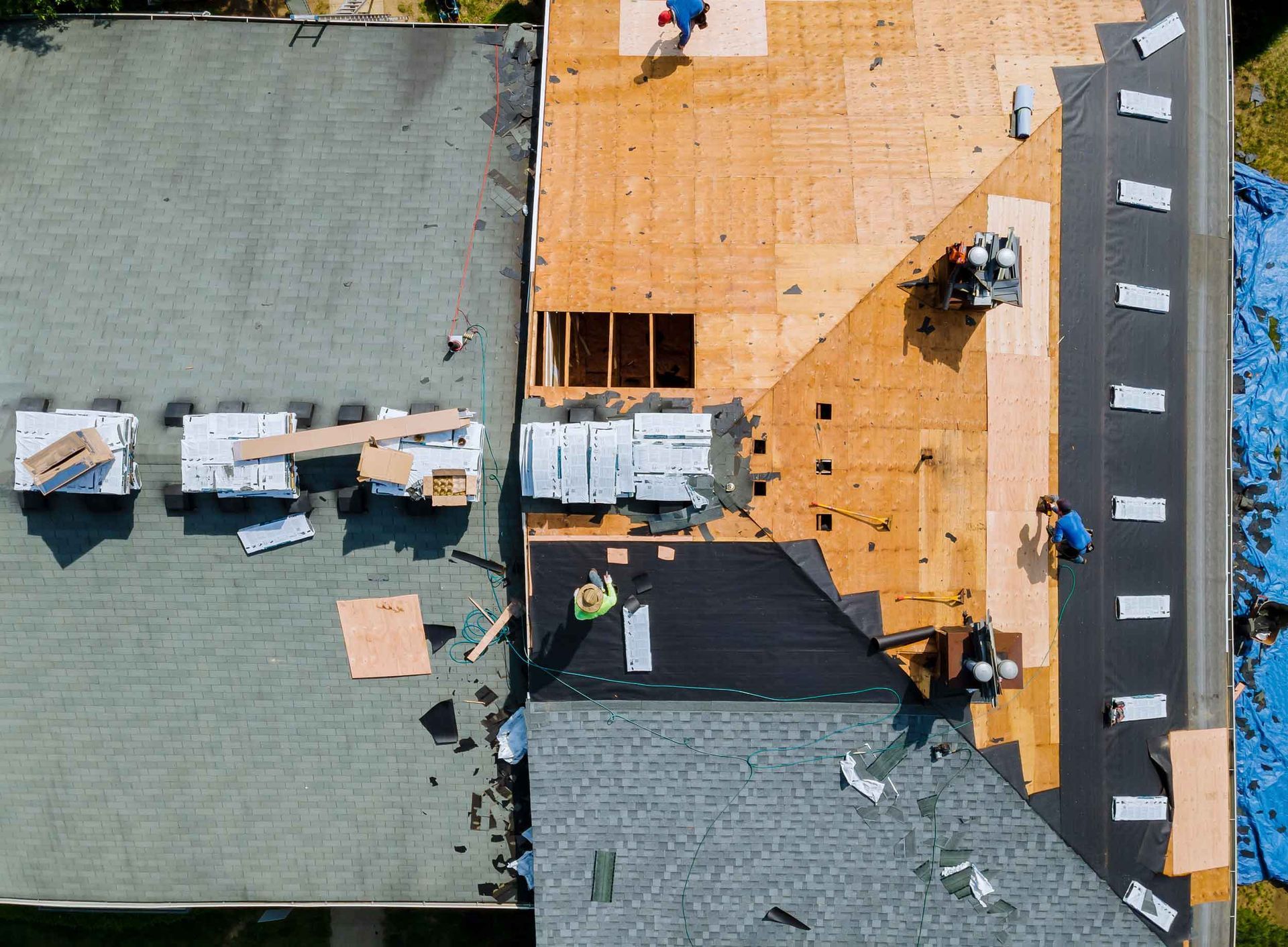 Aerial view of a roof mid-replacement with exposed wood decking and crews installing materials. Aerial view of a roof mid-replacement with exposed wood decking and crews installing materials.