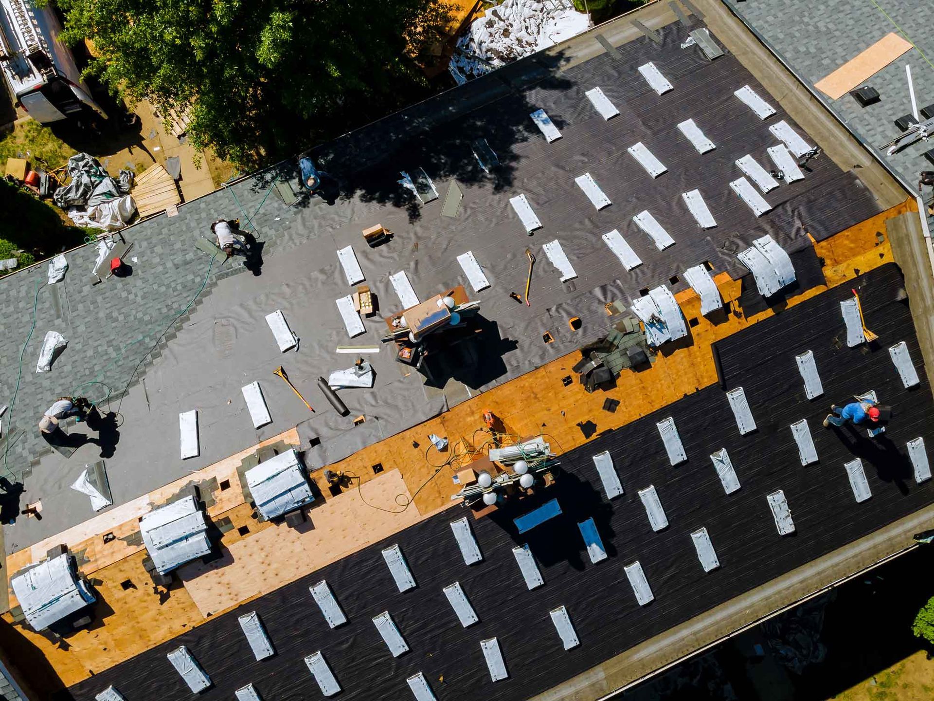 Aerial view of workers installing roofing materials on a large flat residential building roof.