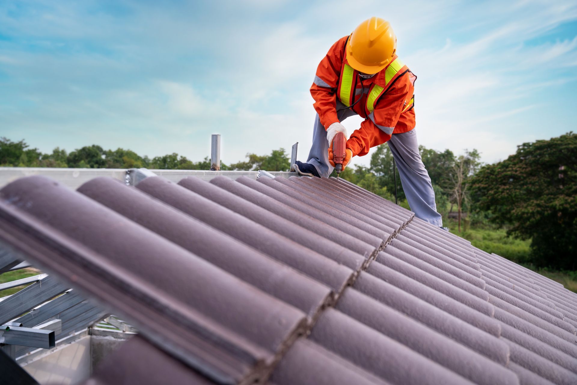 The roofer installs asphalt shingles with a nail gun on a new residential roof.
