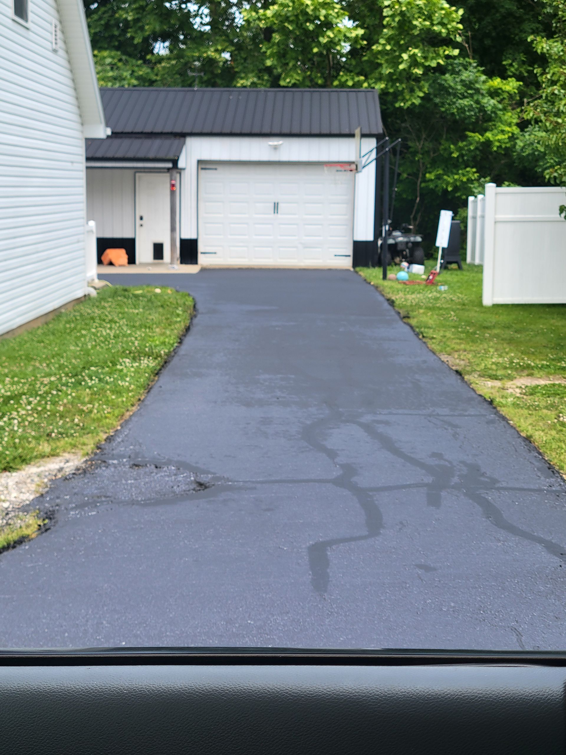Black asphalt driveway leads to a white garage with a black roof. Green grass borders the driveway.