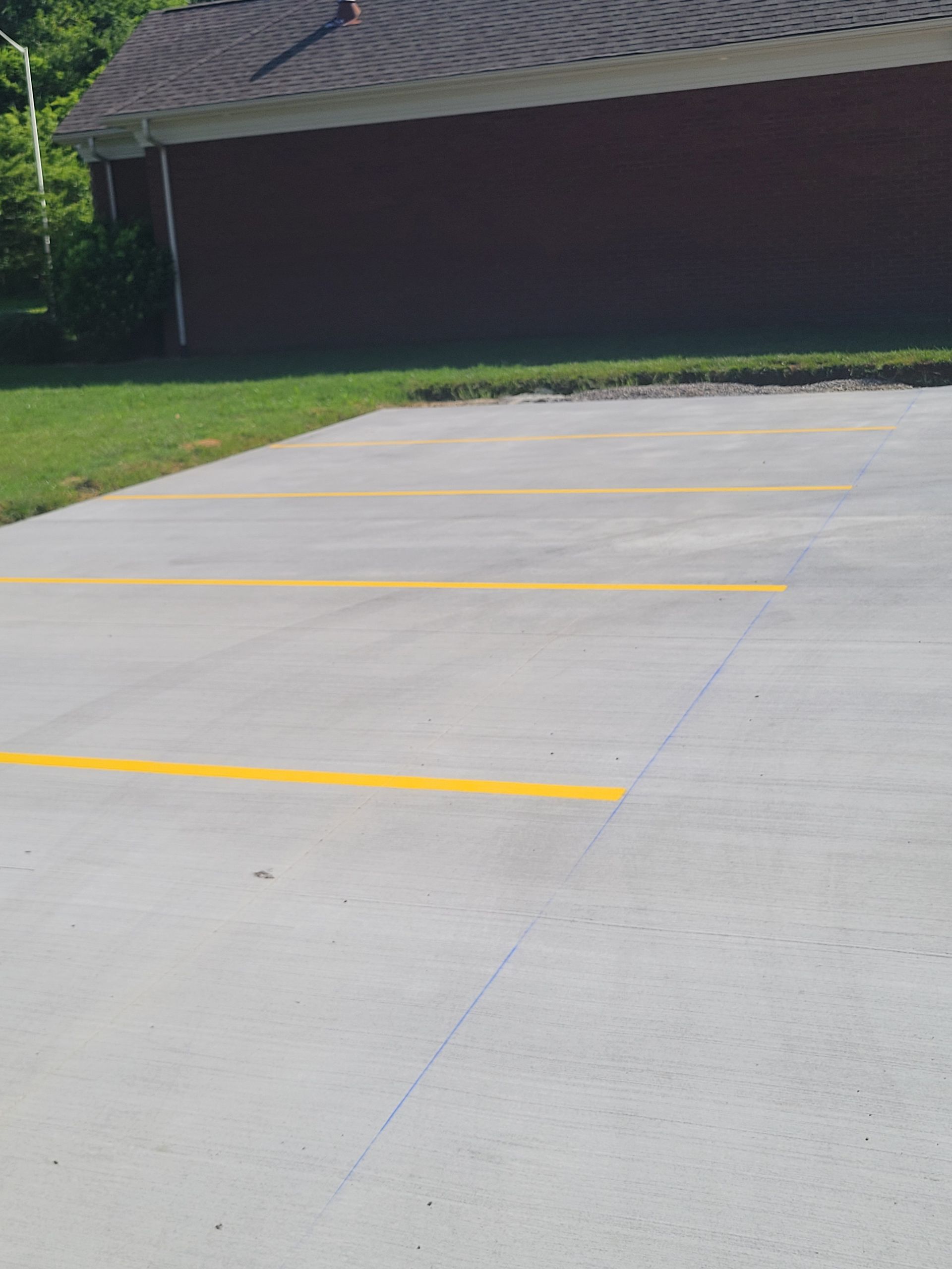 Parking lot with yellow painted lines for spaces.  A dark brick building and green grass are in the background.