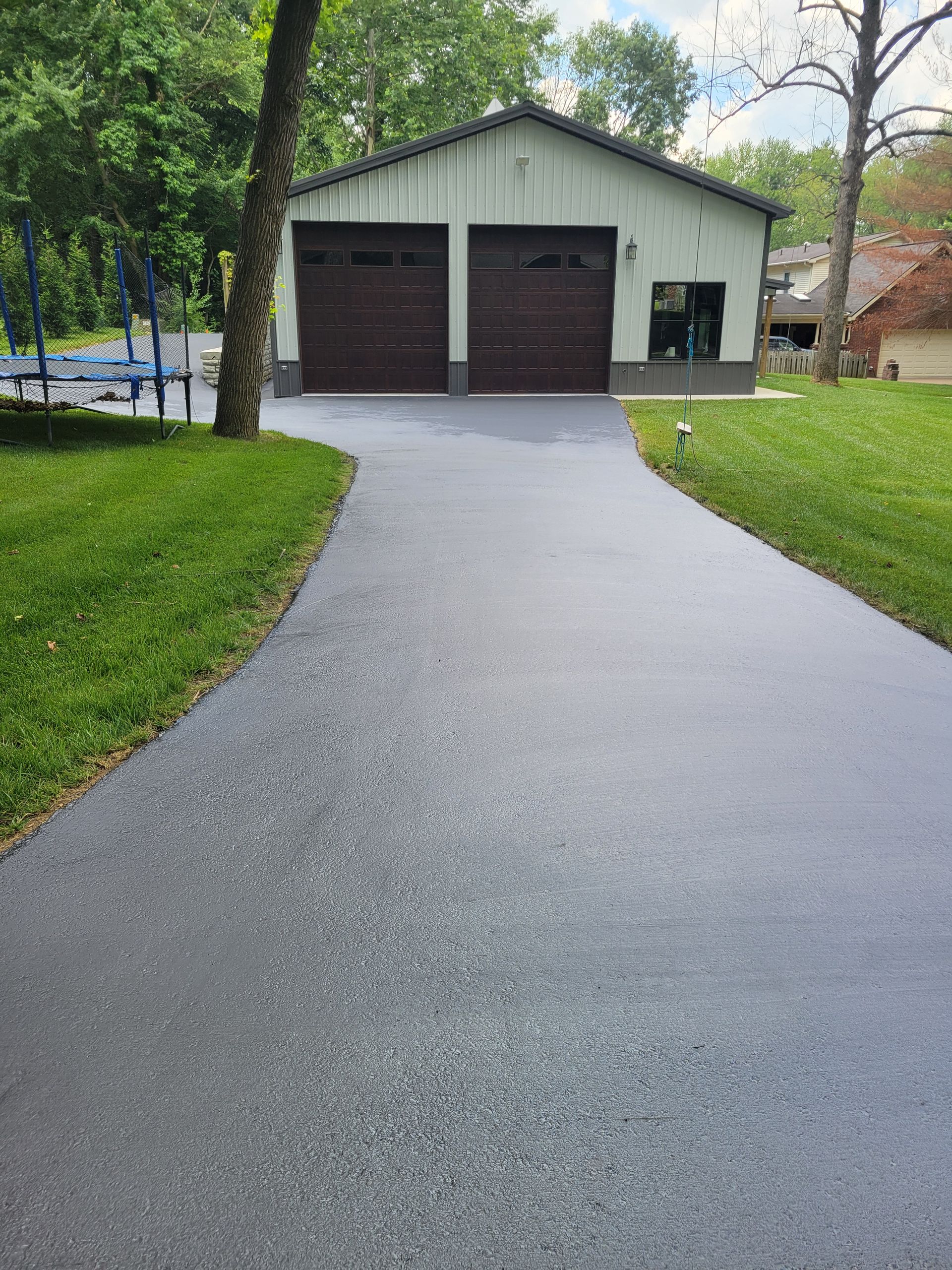 Asphalt driveway leads to a two-car garage with brown doors. Green grass surrounds the driveway.