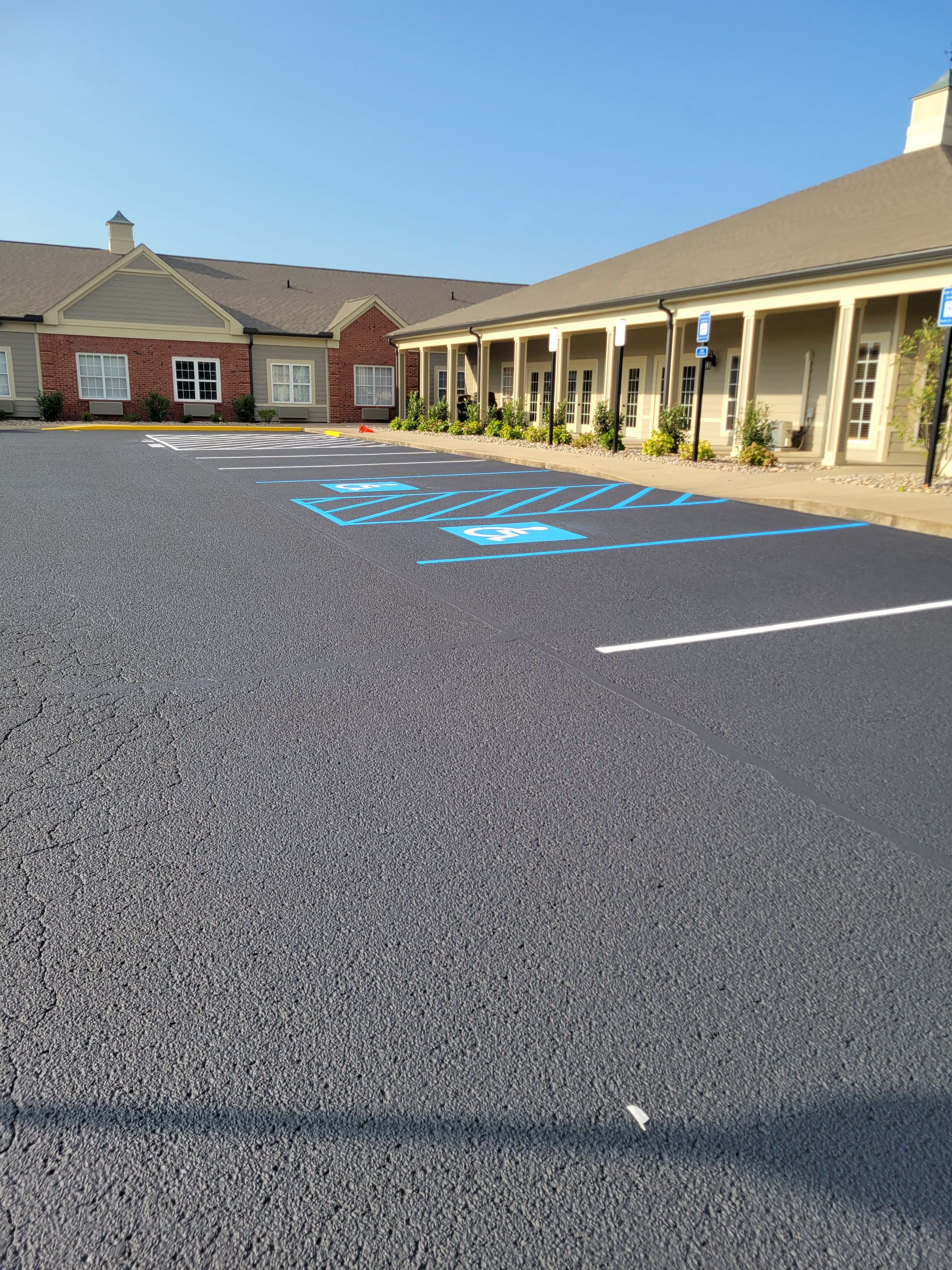 A parking lot with blue handicap parking markings in front of a light-colored building with a red br