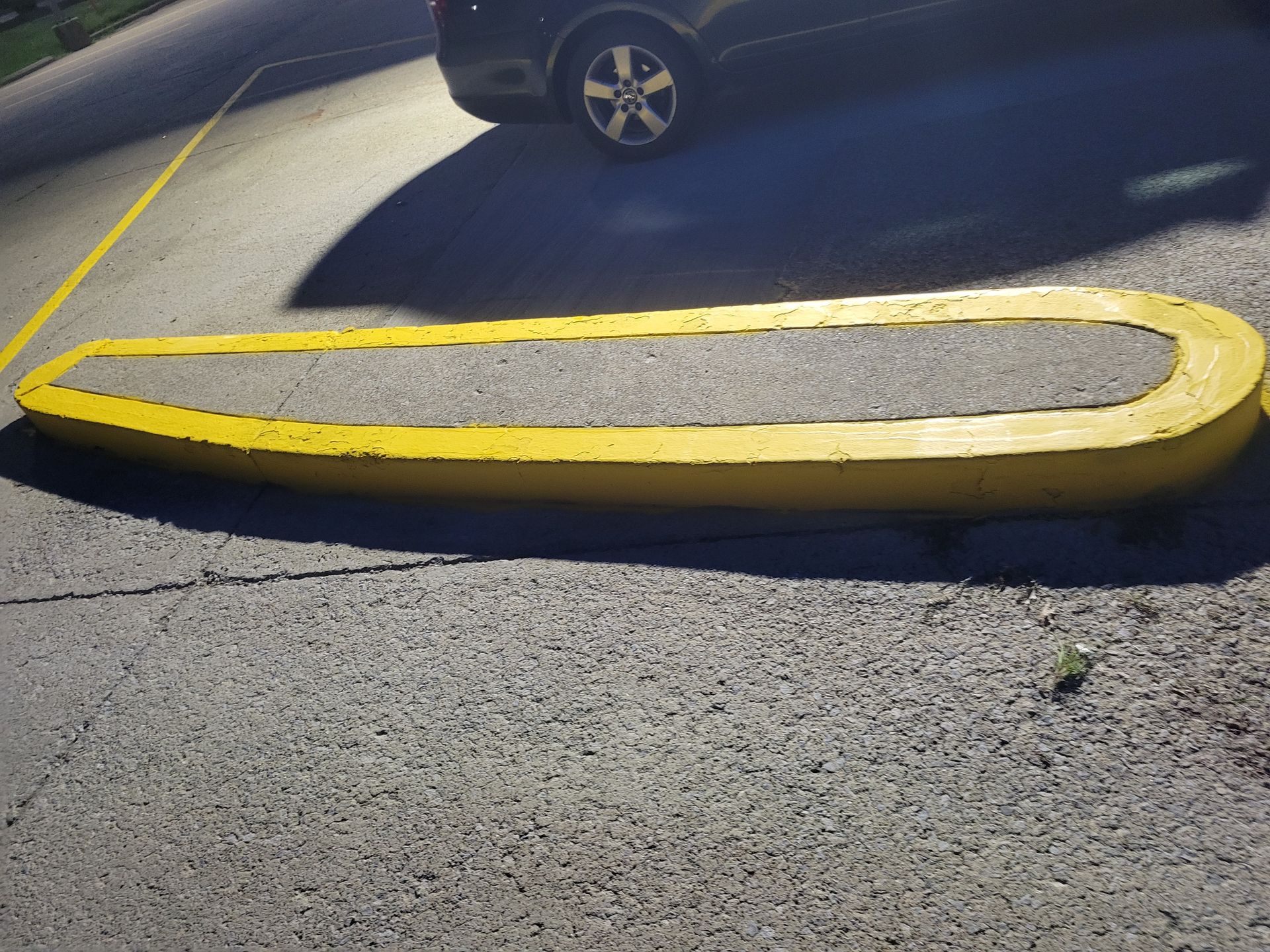 Yellow parking stop on asphalt, with a car's tire visible in the background.