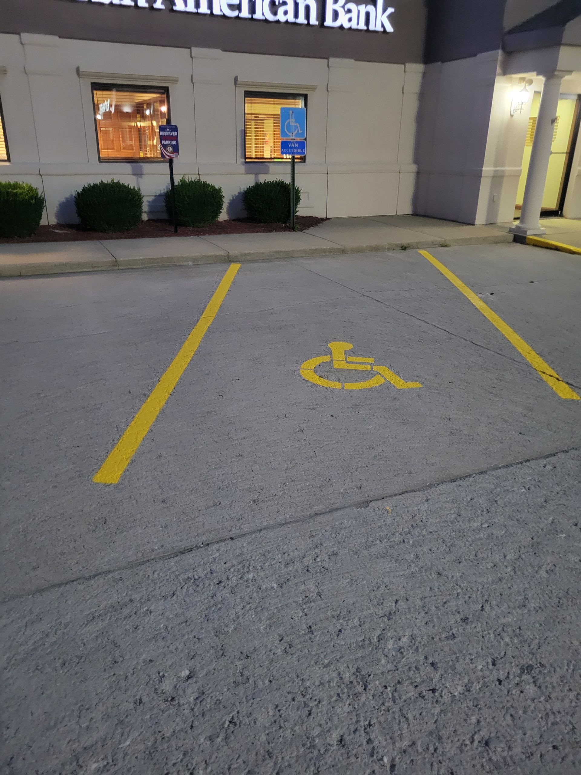 Yellow painted handicapped parking space in front of a bank.  The space is empty, with a wheelchair 