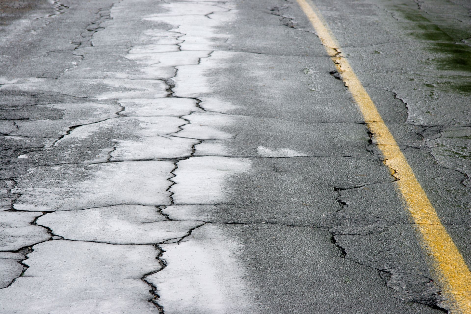 A close up of a cracked asphalt road with a yellow line