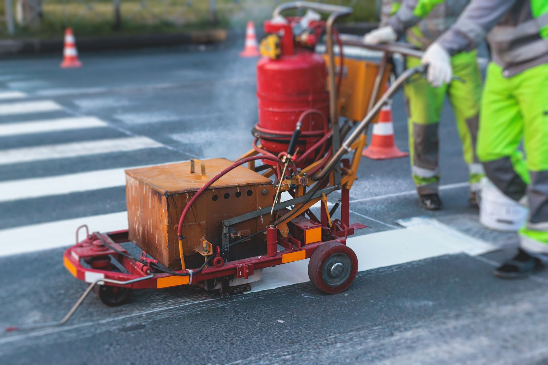 A man is using a machine to paint a crosswalk on the road.