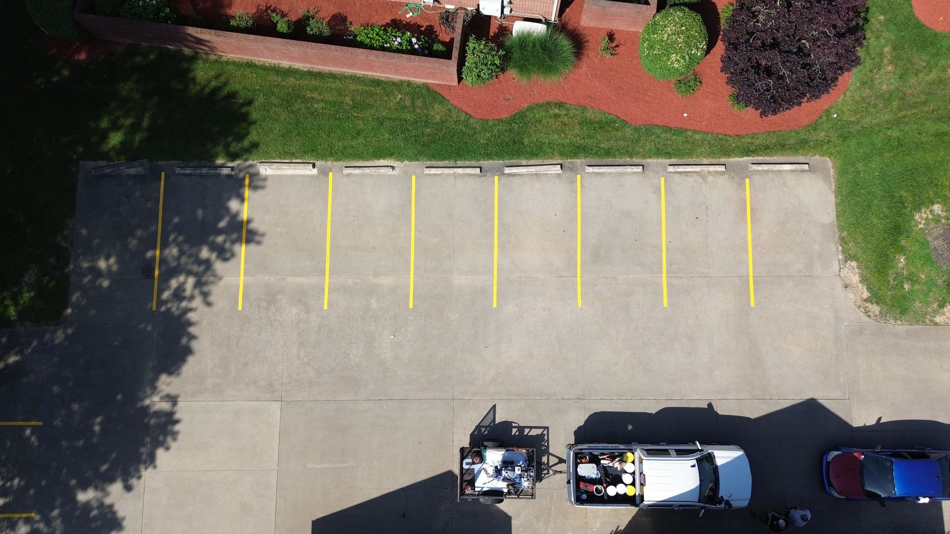 Overhead view of a parking lot with yellow lines. A white work van and other vehicles are parked.