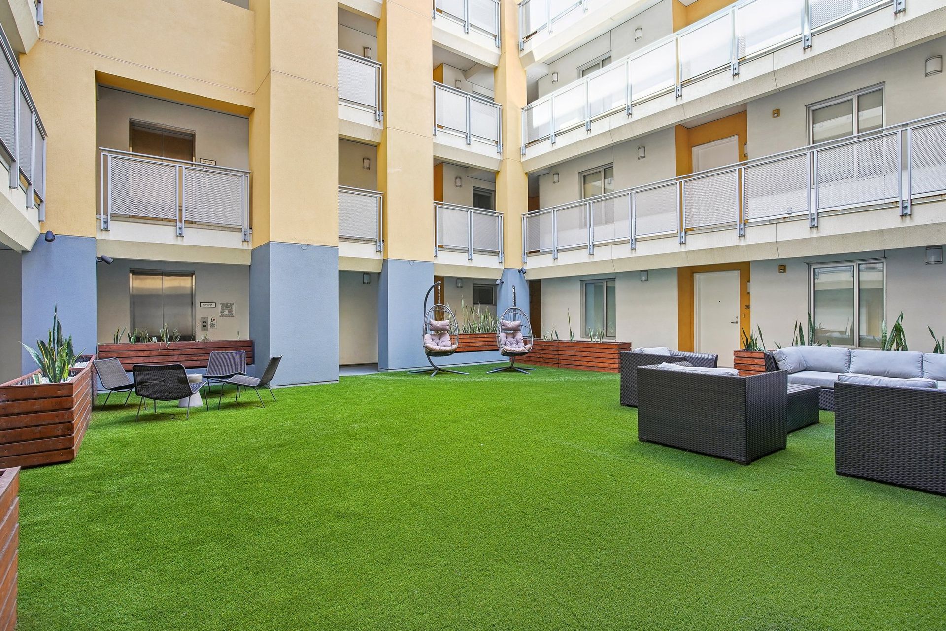 A courtyard with artificial turf, seating areas, and balconies on surrounding building.