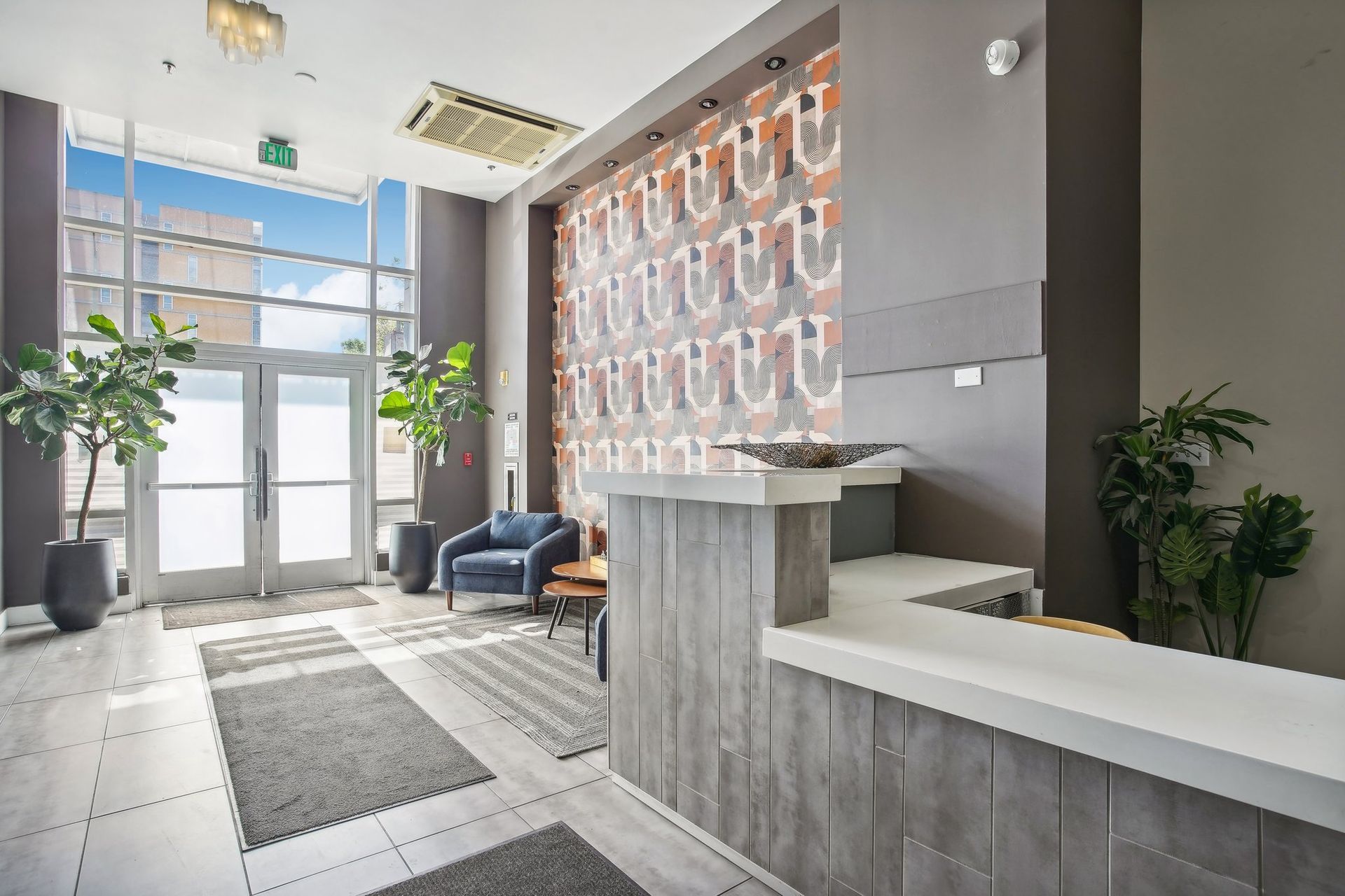 Reception area with a desk, patterned wall, plants, and glass doors.