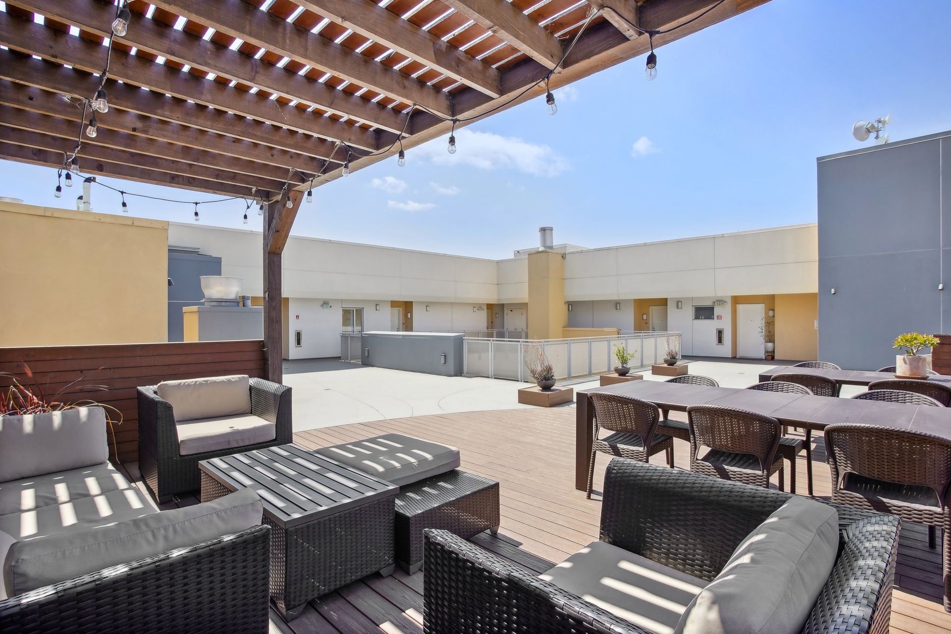 Rooftop patio with lounge seating under a pergola and dining tables. White walls, blue sky.