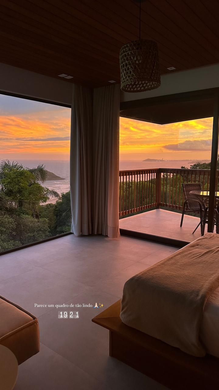 Um quarto luxuoso com vista panorâmica para um pôr do sol vibrante sobre o oceano e uma varanda privativa de madeira.