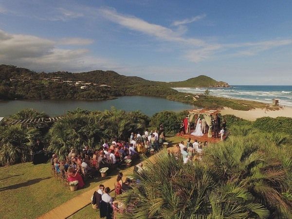 Uma cerimônia de casamento ao ar livre com vista para uma lagoa costeira e praia, com os convidados sentados na grama.