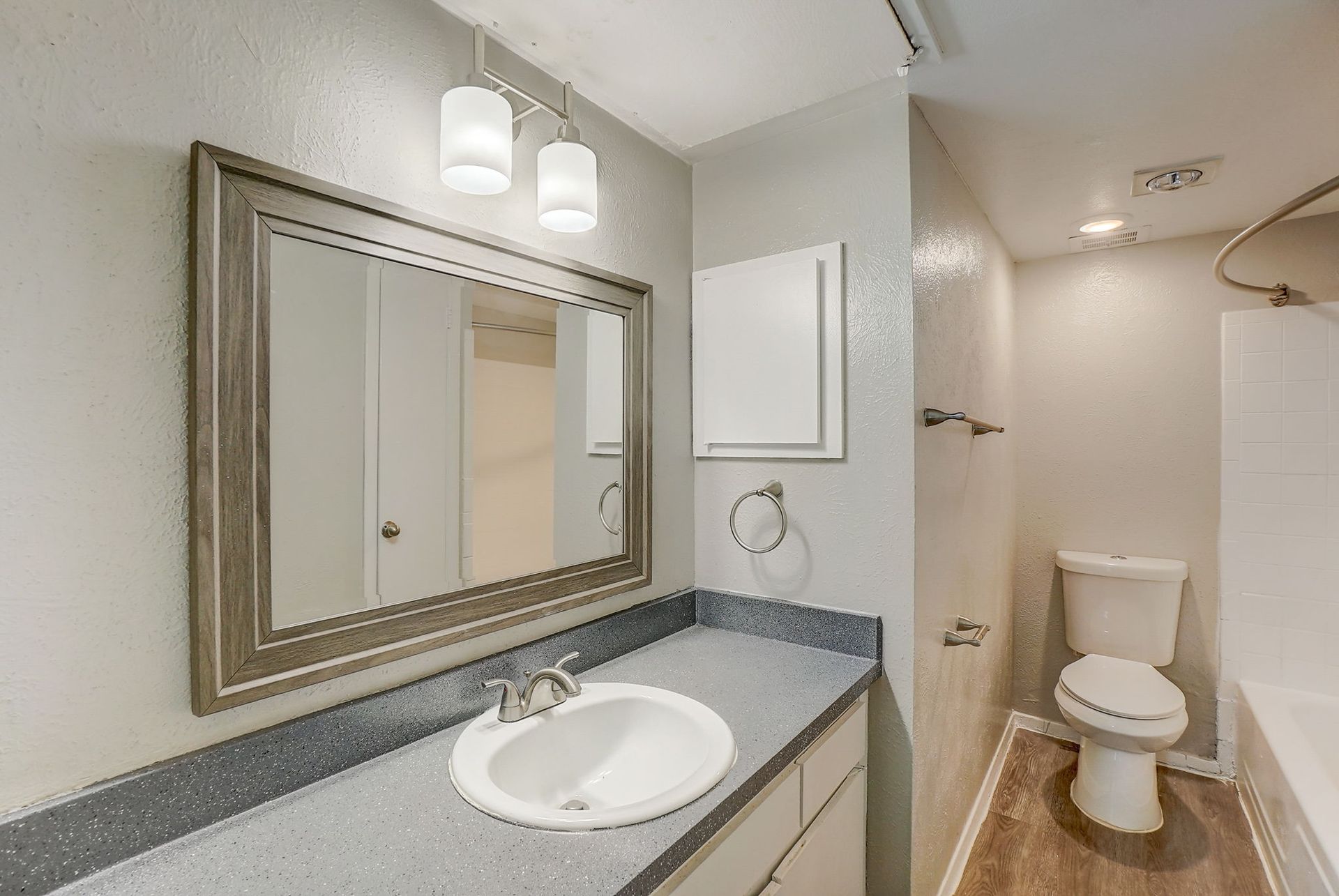 Bathroom with a gray countertop, white sink, and large mirror. Toilet and shower visible.
