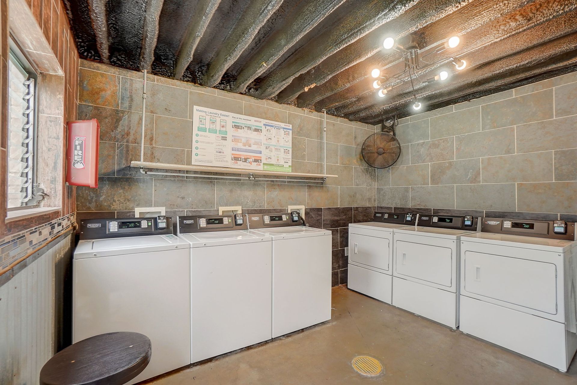 Laundry room with multiple washing machines and a dryer. Gray concrete walls, utility.