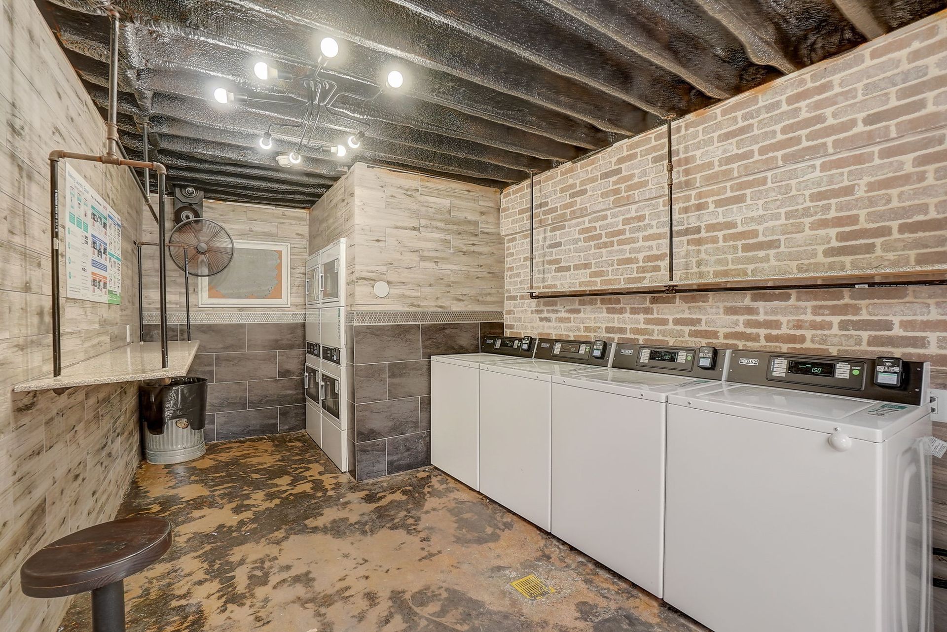 Laundry room with brick walls, washing machines, and a stool.