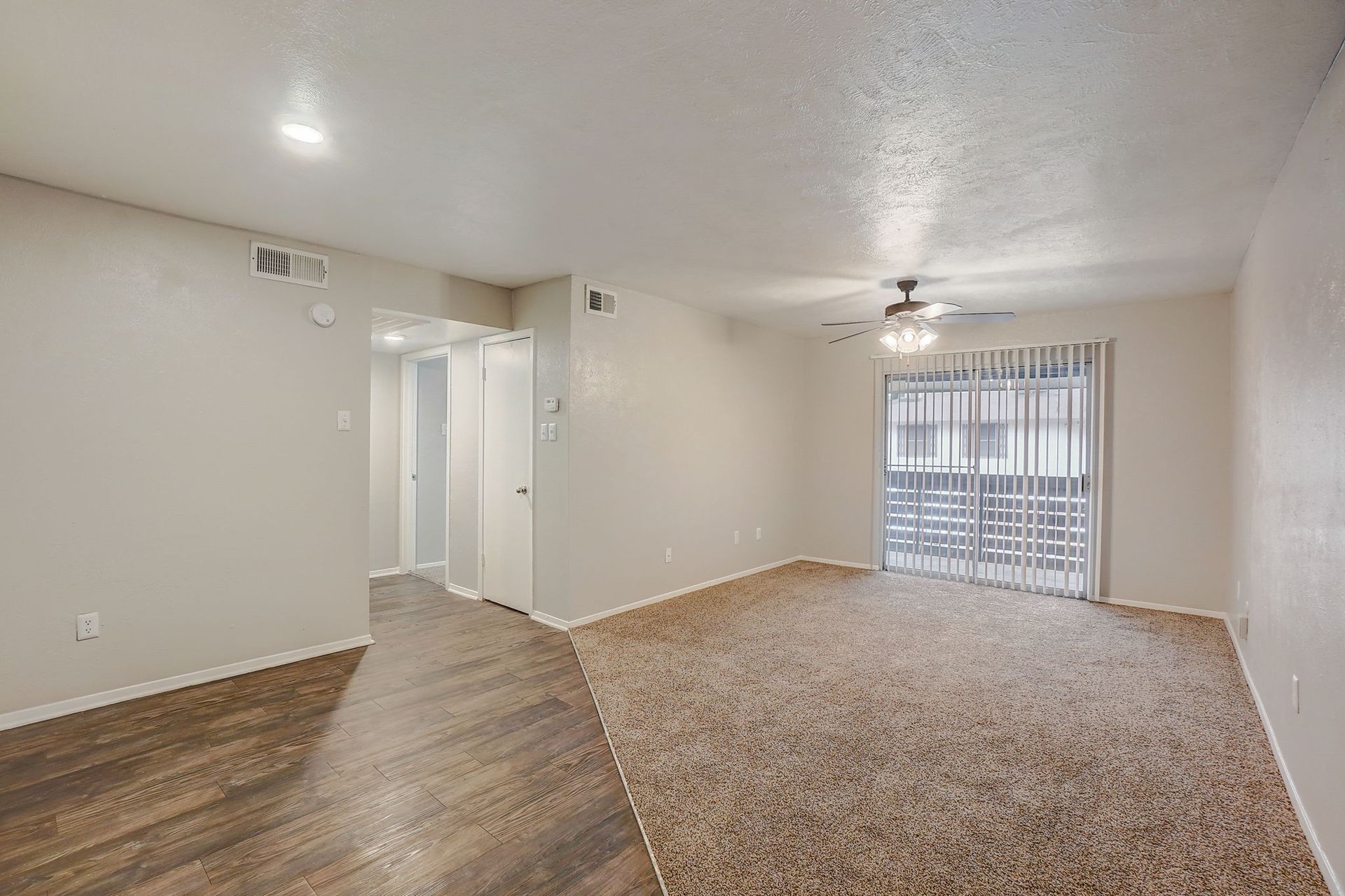 Empty living room with tan carpet and sliding glass door leading to a balcony.