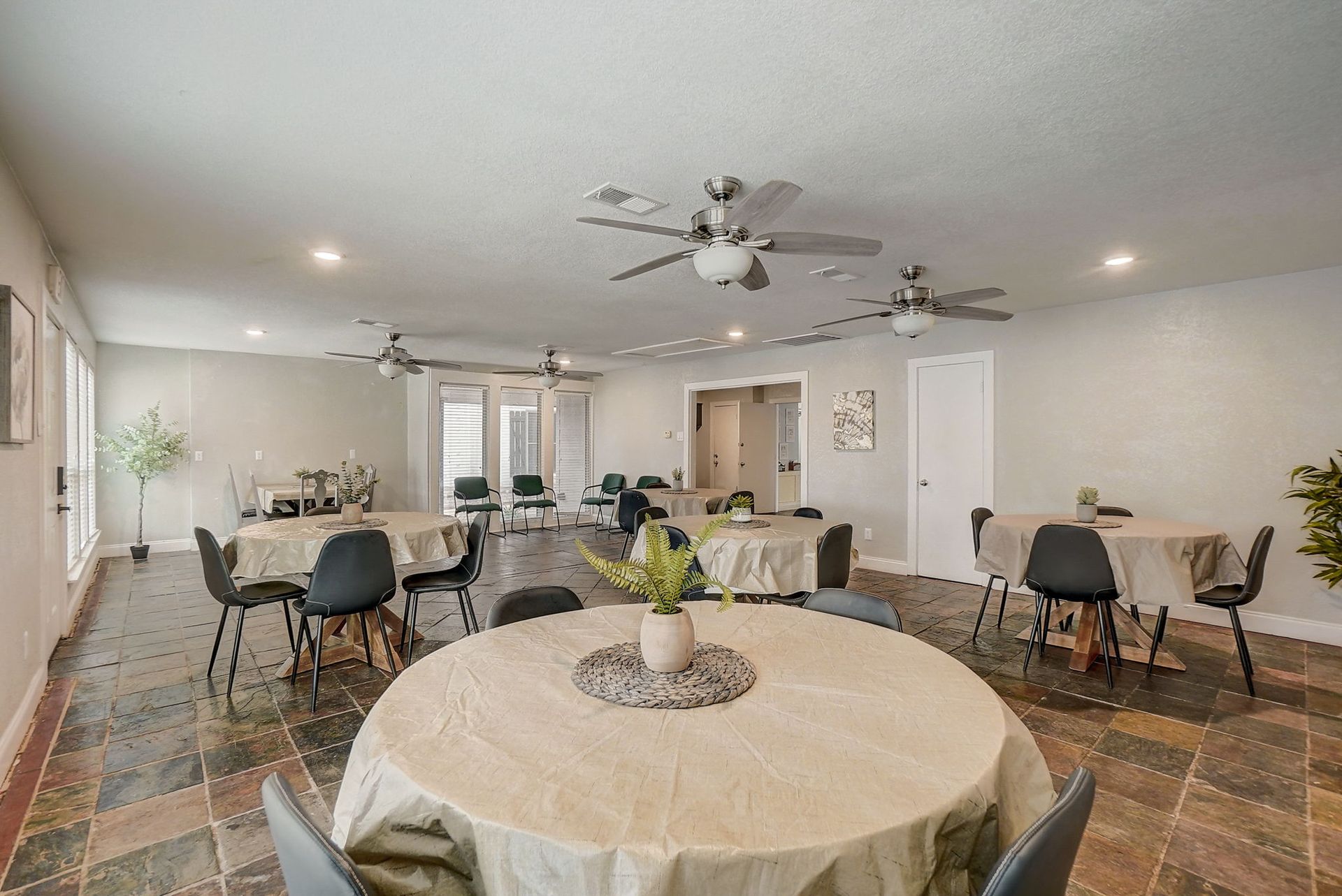 Interior of a banquet hall with round tables covered in beige cloths, surrounded by black chairs.