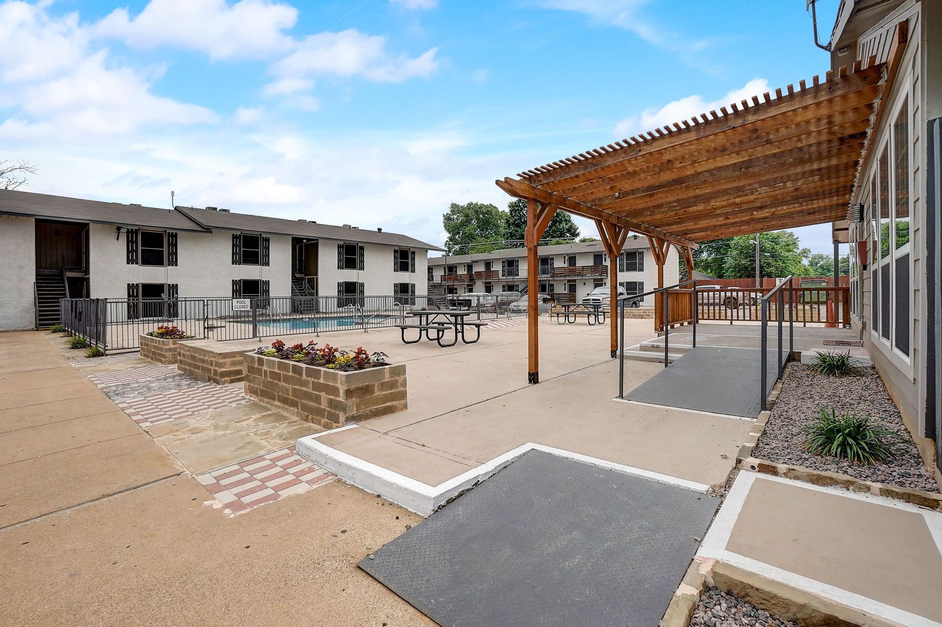 Courtyard with pergola, seating, pool, and apartment buildings under a blue sky.