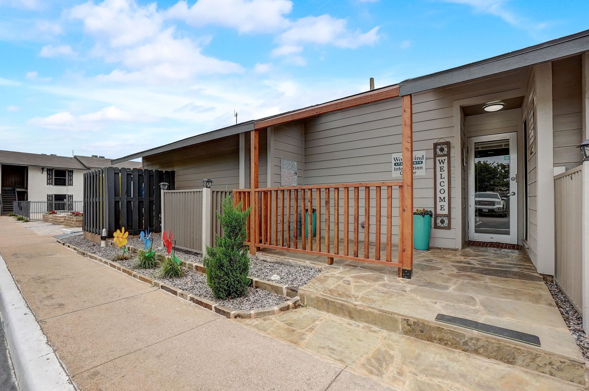 Exterior view of a small townhouse with a front porch, brown and grey tones, pathway.