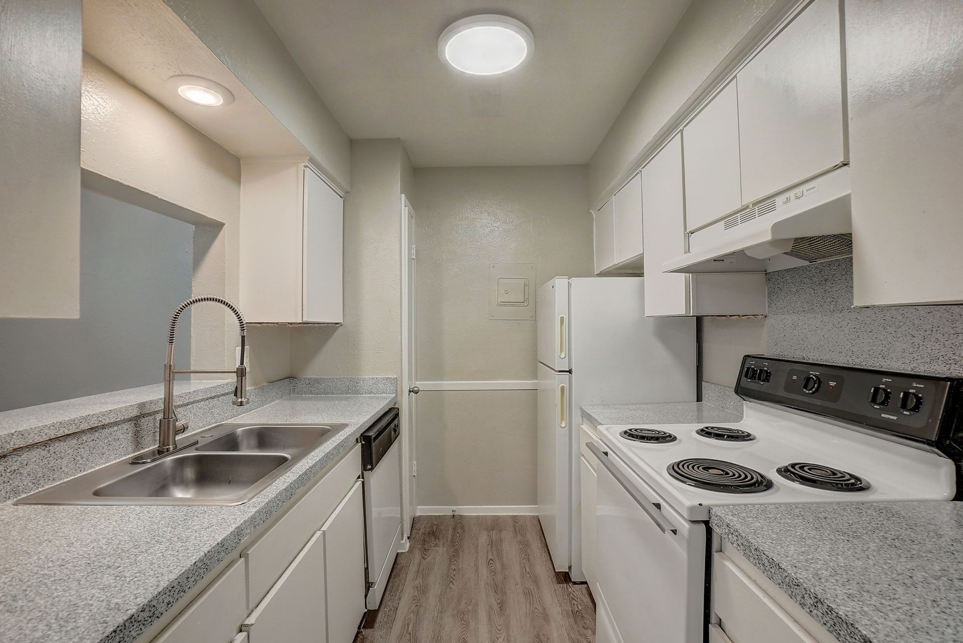 Kitchen with white cabinets, speckled countertops, stainless steel sink, and a white refrigerator.