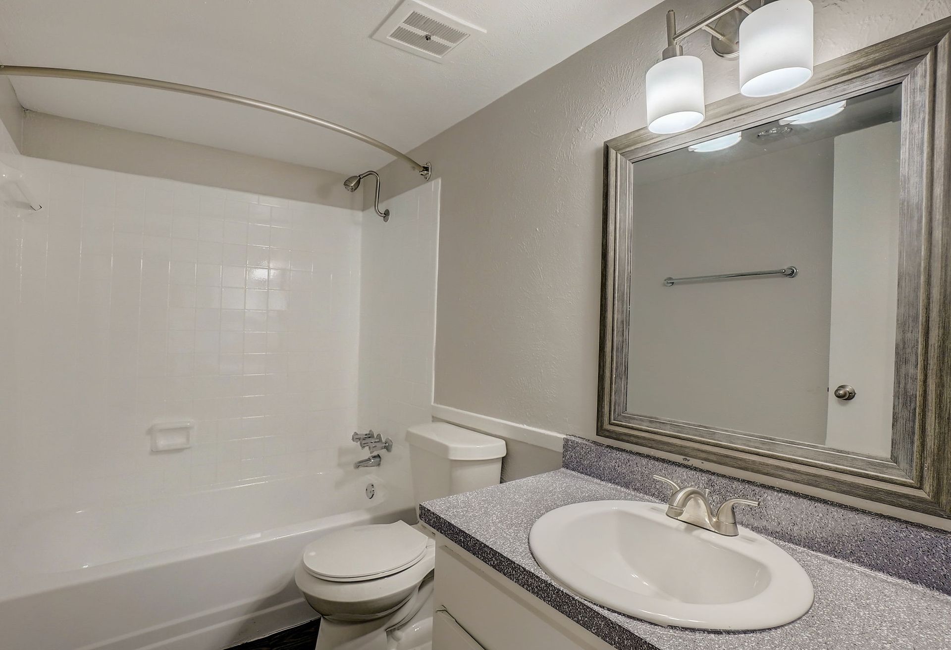 Bathroom with white tile, vanity with oval sink, large mirror, and shower/tub combo.