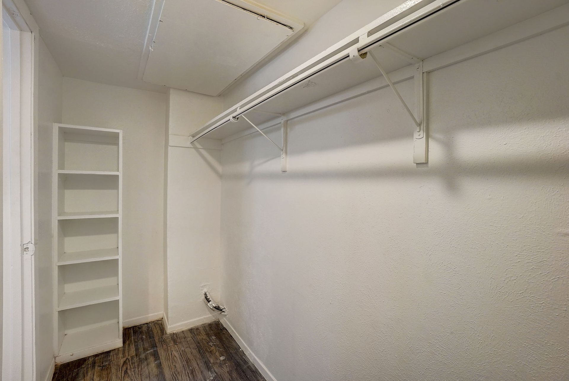 Empty closet with white shelving and wire rack, white walls, and dark flooring.